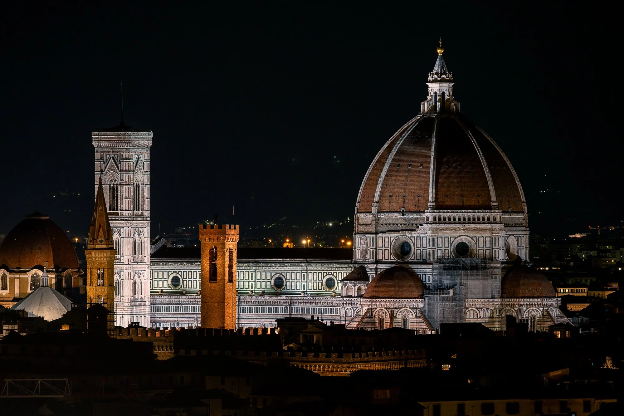 De Duomo di Firenze bij nacht, met de koepel en de Campanile di Giotto verlicht tegen een donkere hemel.