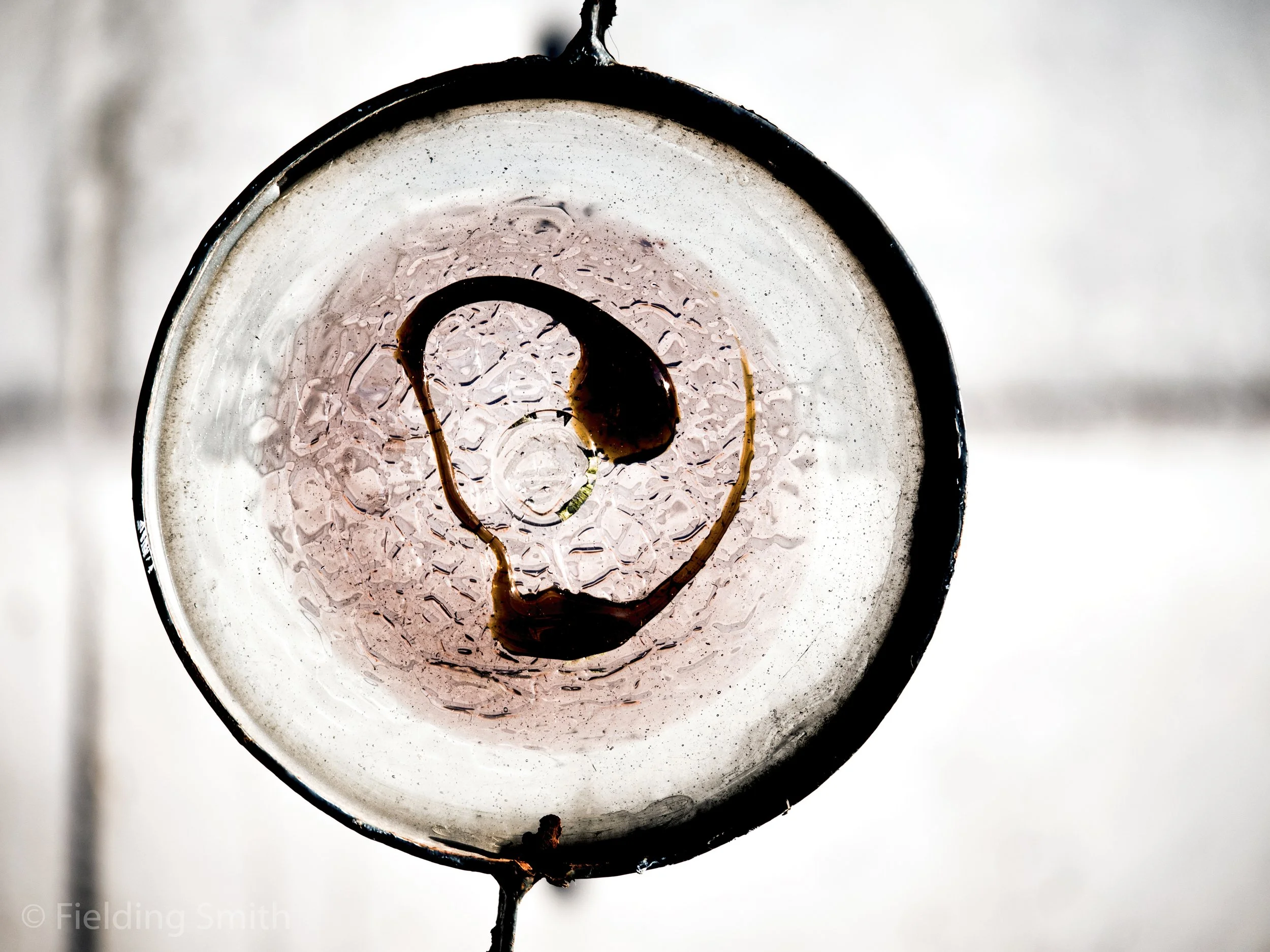 A top-down view of a glass with condensation on the inside, containing a dark liquid and ice, with a smiley face created by the liquid and ice.