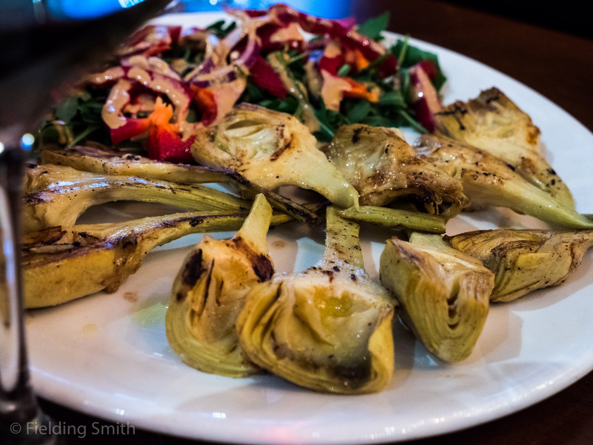 Grilled artichokes served with a side of mixed greens and chopped vegetables.