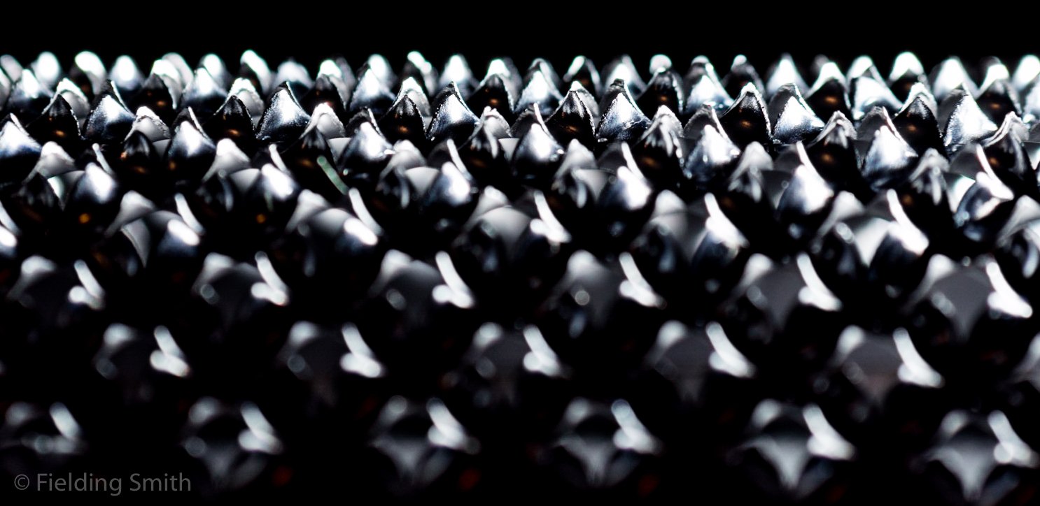 Close-up of a black surface with numerous metallic spikes protruding upwards.