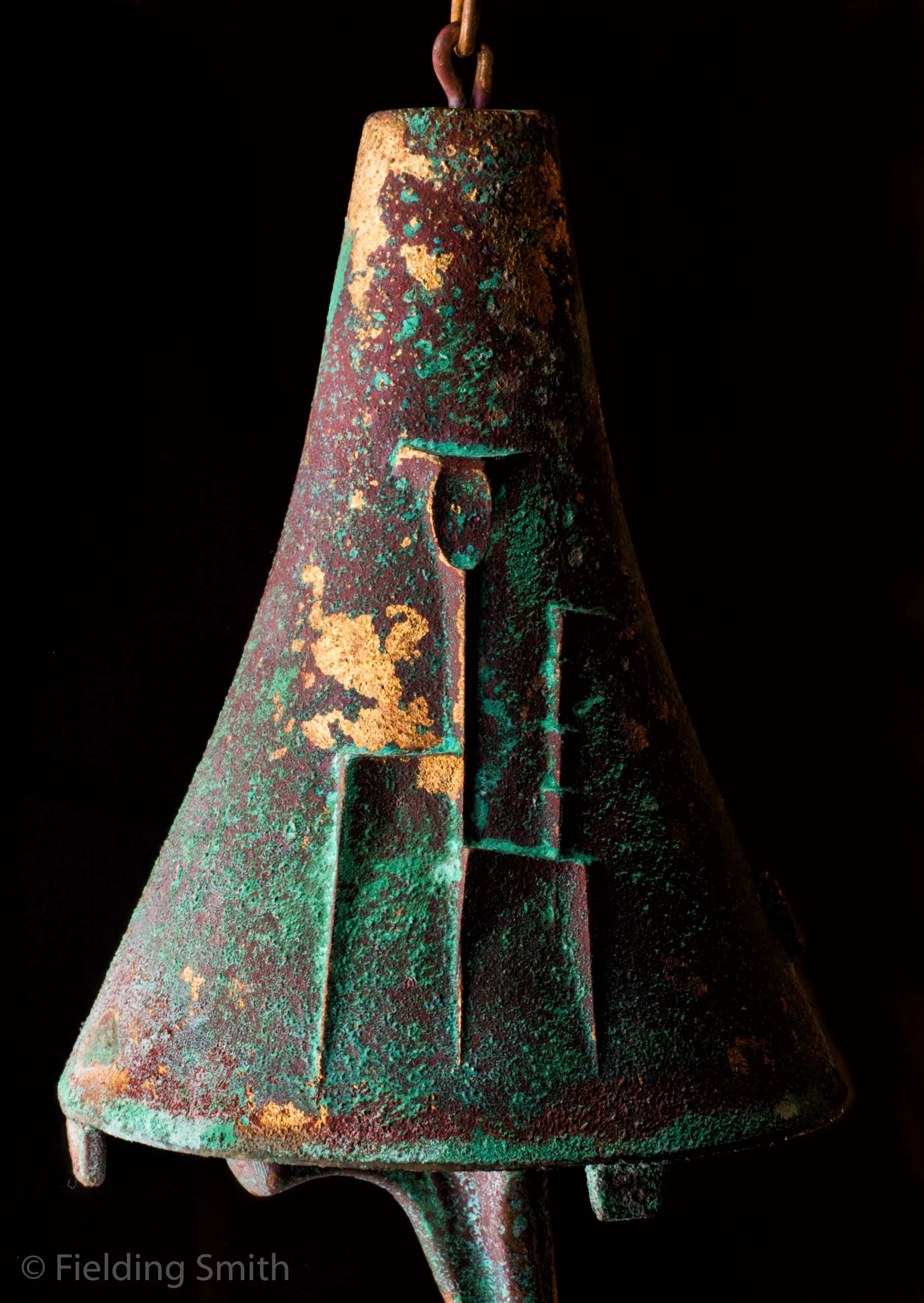 Close-up of a weathered, greenish and brown bell against a black background.