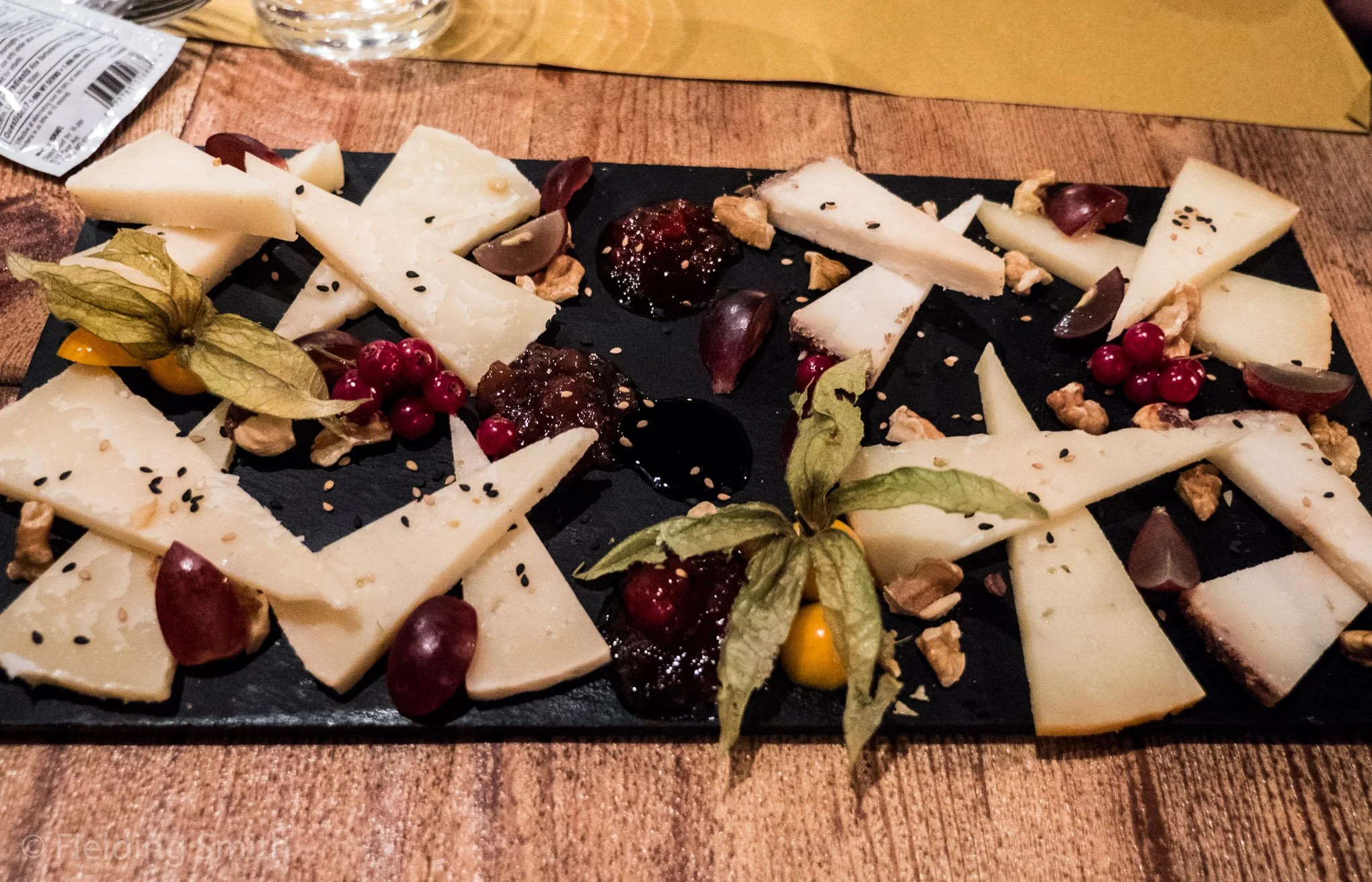 Cheese platter with various cheeses, grapes, nuts, and berries on a black serving board.