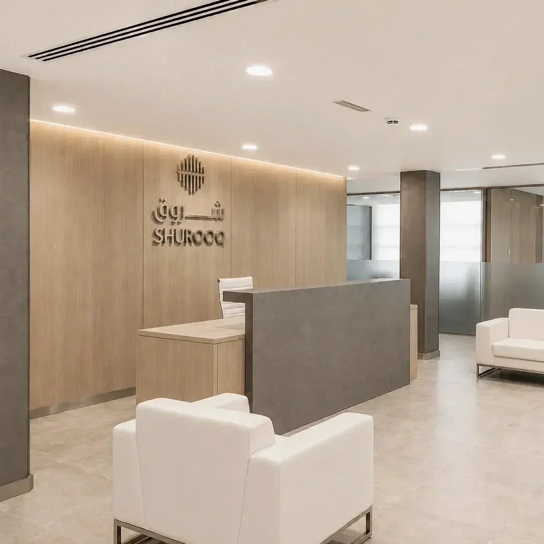 Modern office reception area for Shurooq at Qanat Al Qasba Sharjah featuring desaturated oak finishes, frosted glass partitions, and minimalist seating.