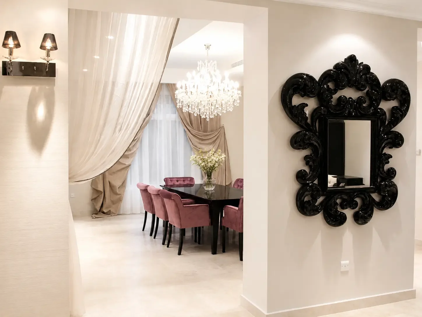 Luxury villa dining room framed by draped curtains and sculptural black mirror with soft neutral interior styling.