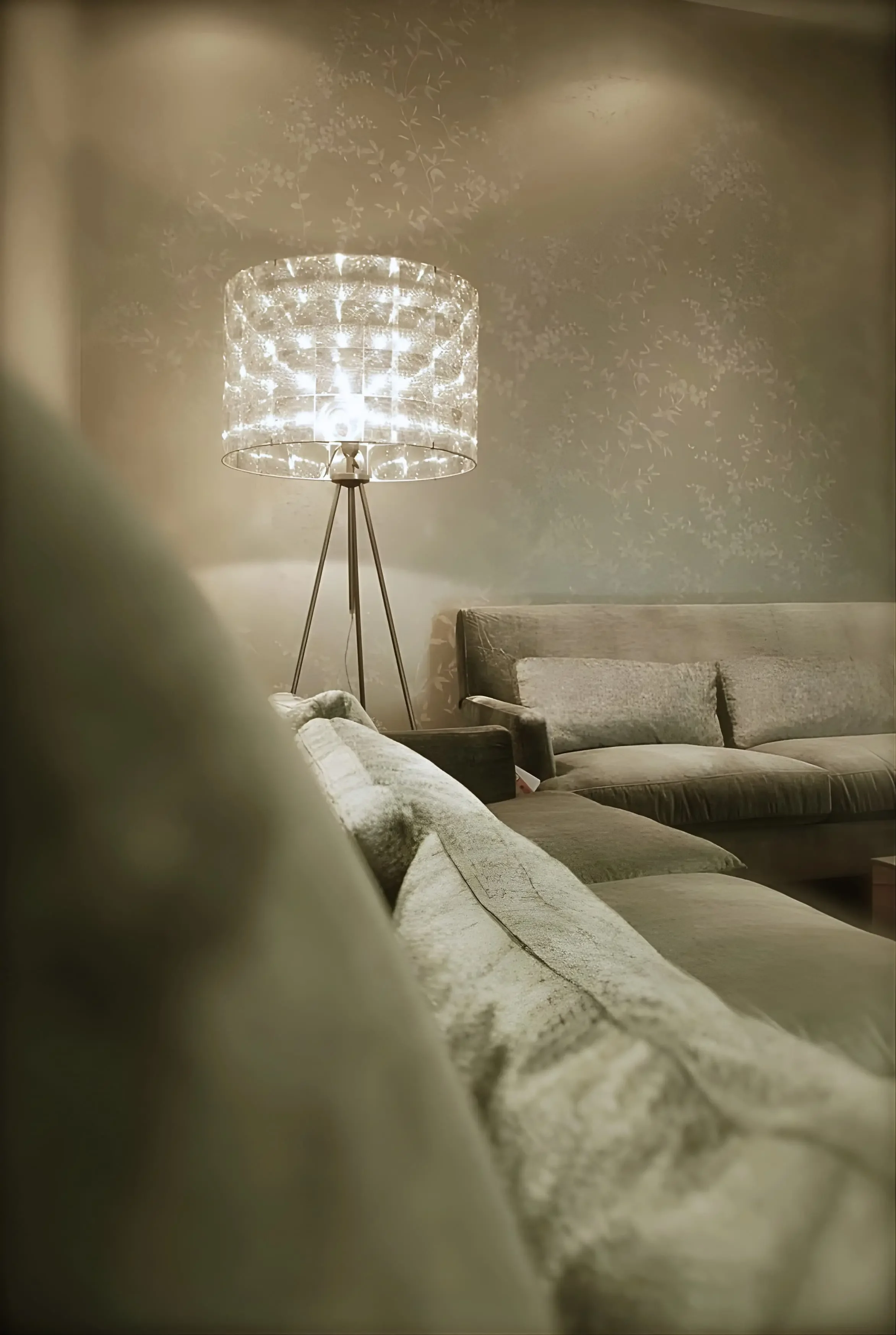 Editorial living room detail with neutral sofas, layered cushions, floral wallpaper, and sculptural crystal floor lamp.