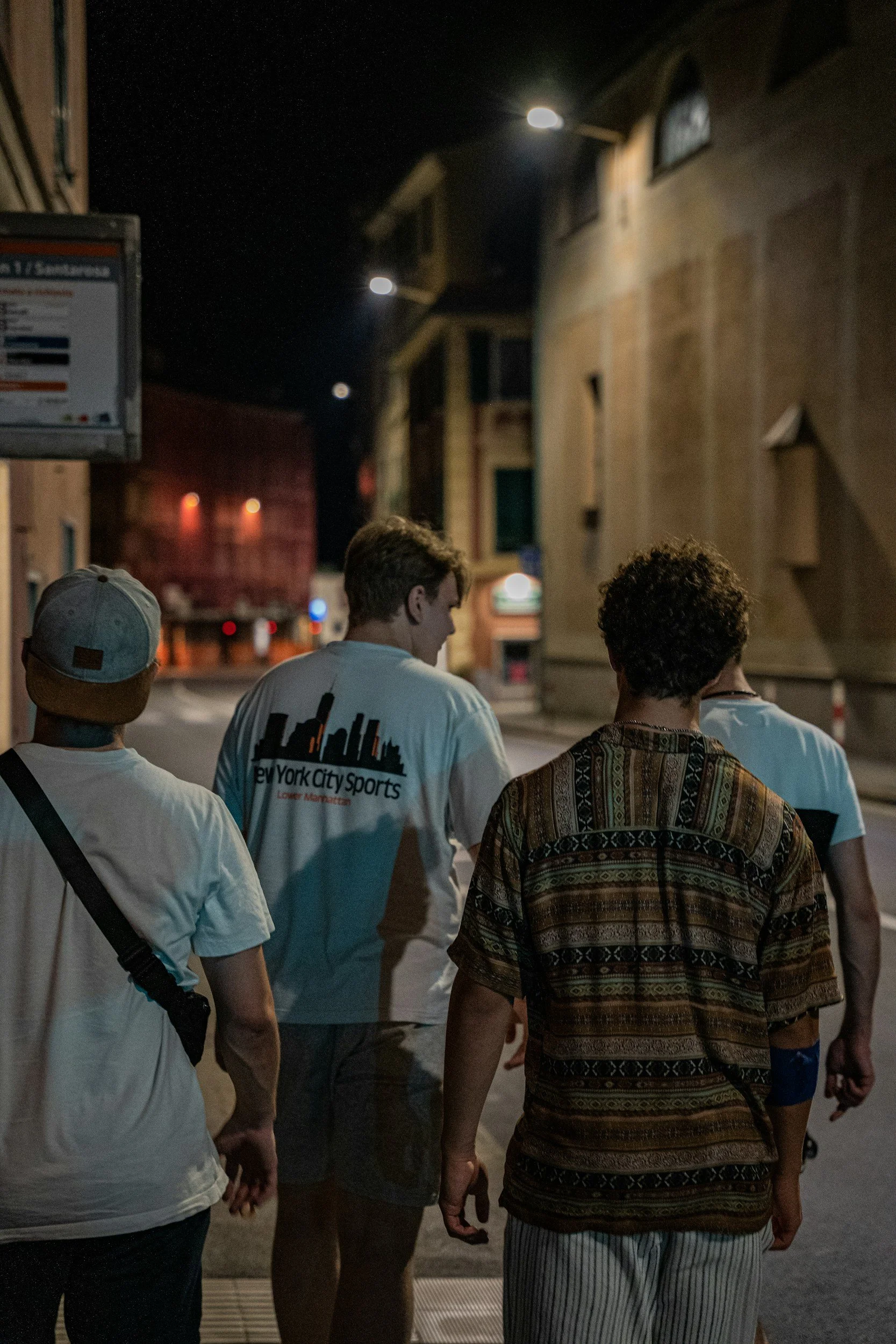 Four people walking on the street at night, with buildings and streetlights in the background.