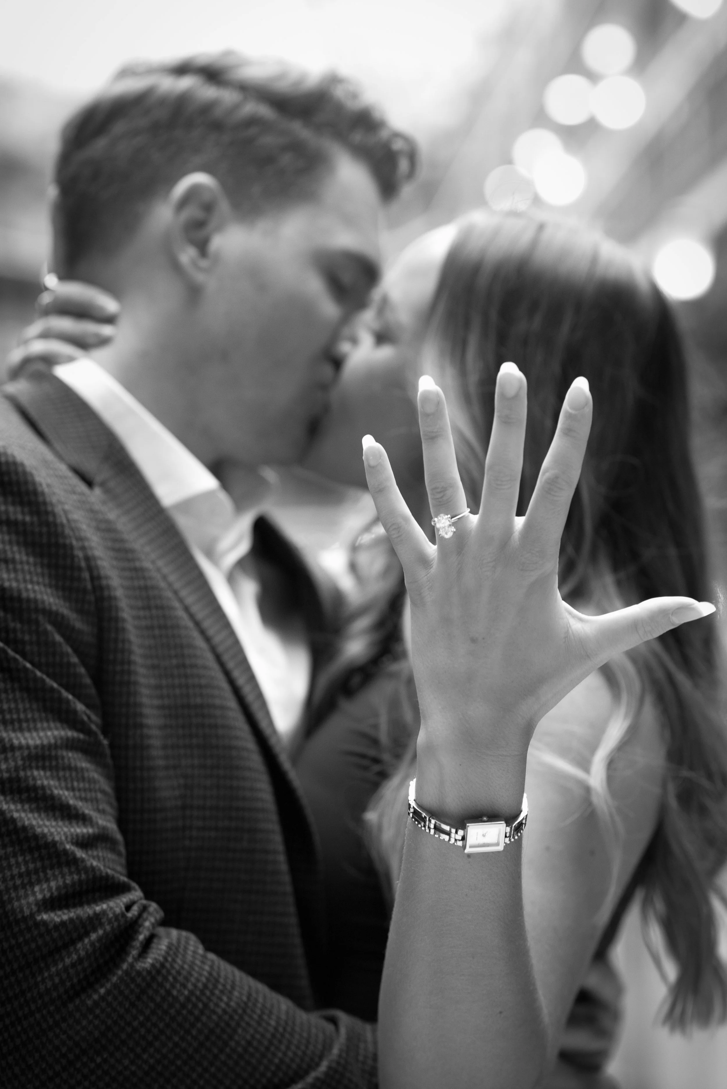 A black-and-white photo of a couple kissing, with the woman's hand prominently displayed showing an engagement ring.