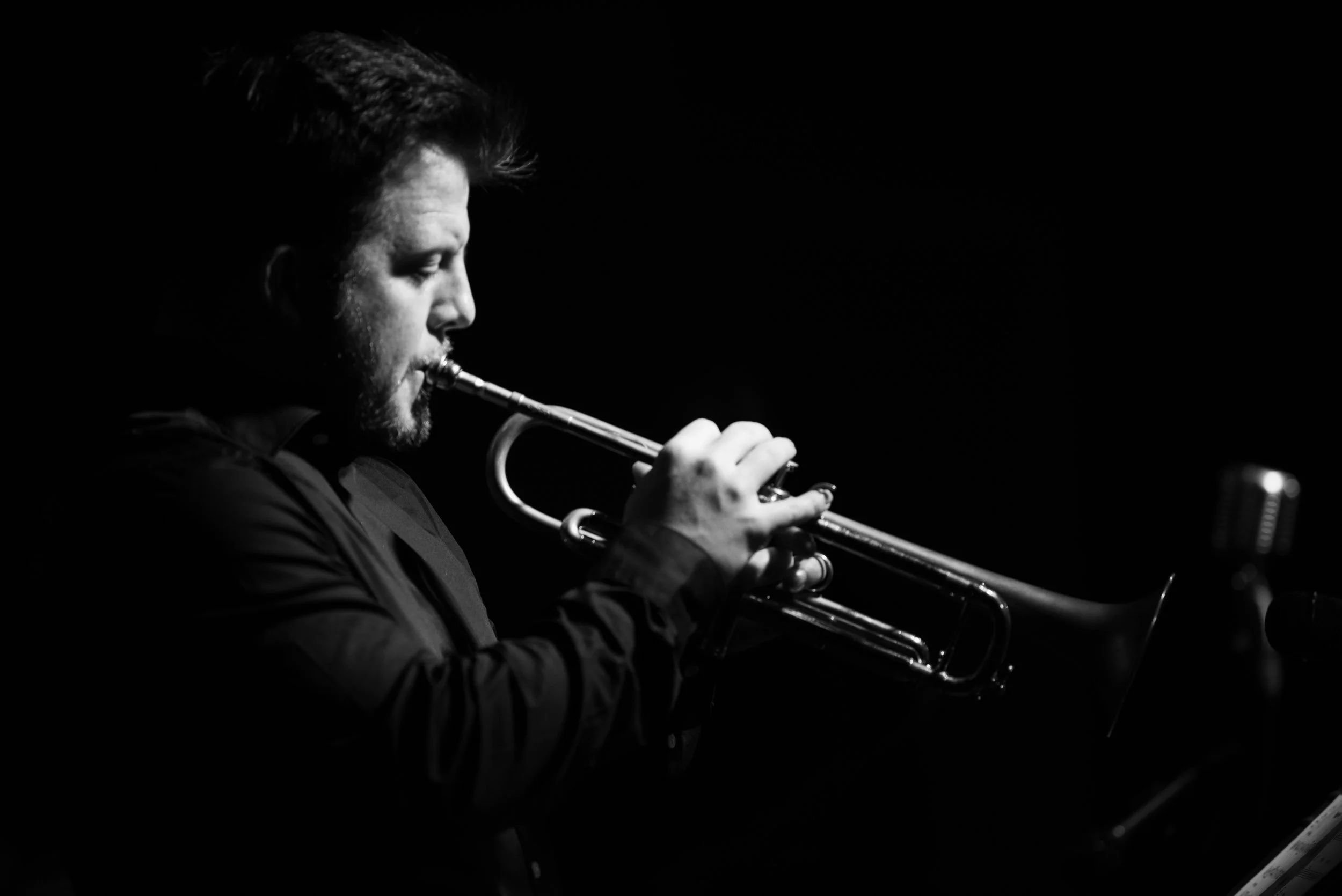 A black and white photo of a man playing a trumpet in a dark setting.