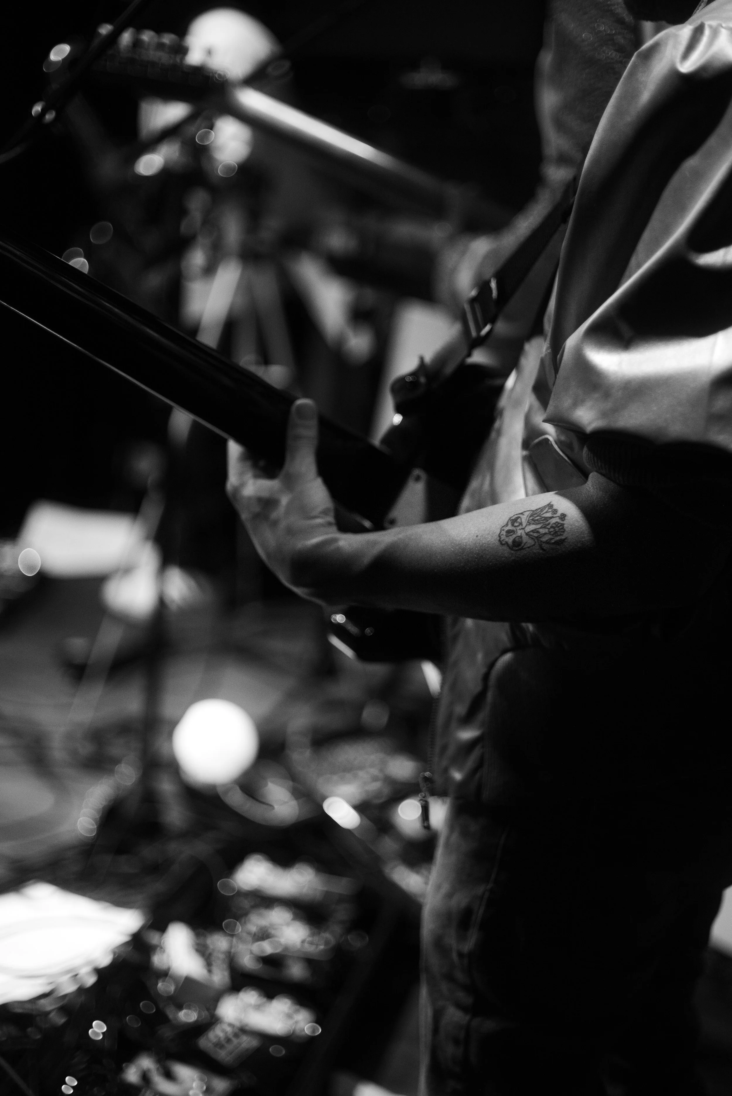 A person playing an electric guitar, with a tattoo of a lion on their arm, in a dark, indoor setting.