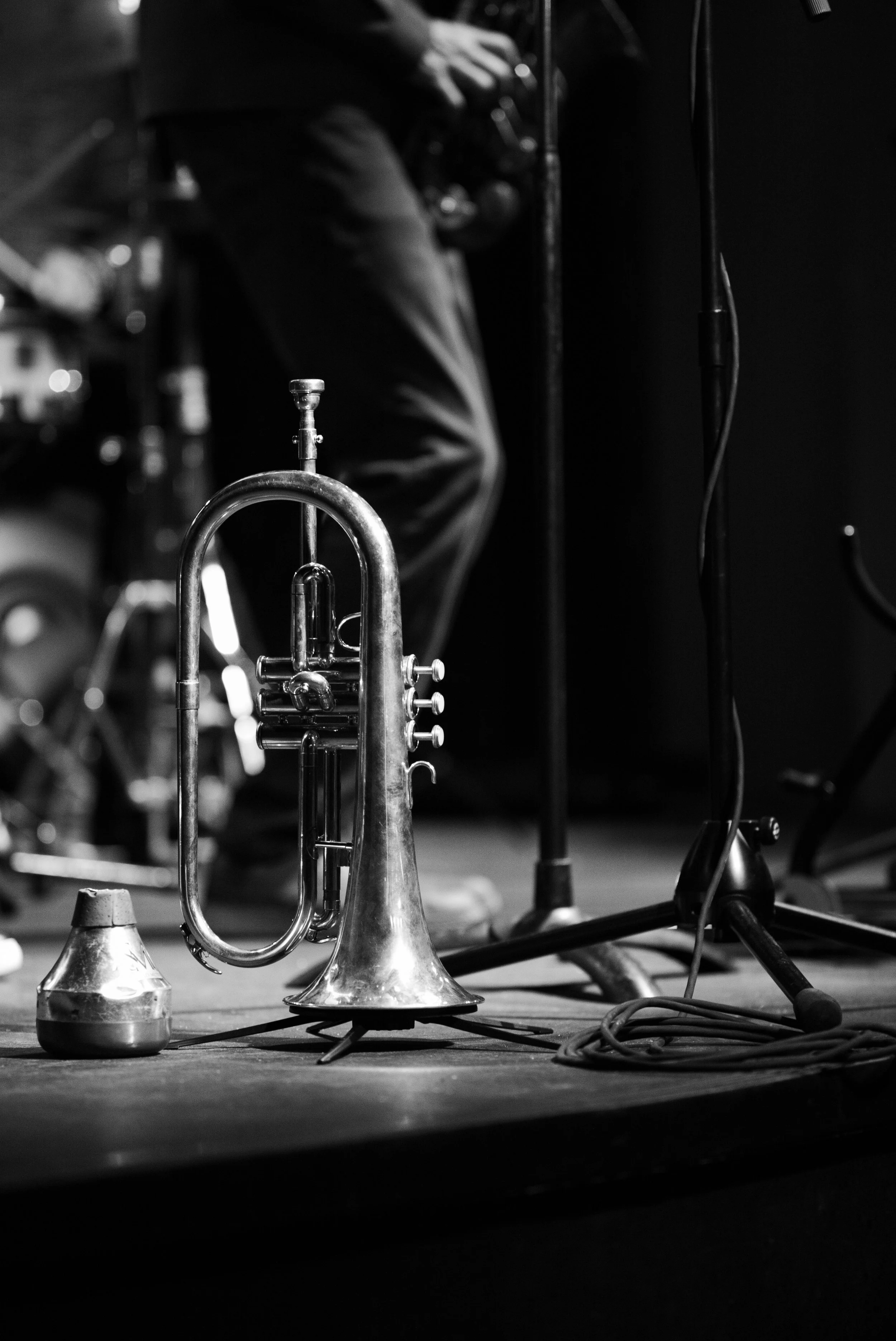 A trumpet placed on a stage with a microphone and a person's legs in the background.