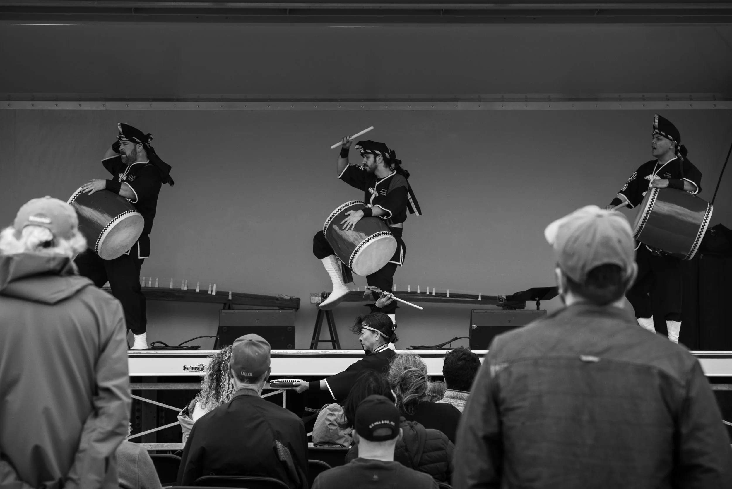 Three musicians dressed as pirates perform a traditional dance with drums on a stage, villagers watch from the audience.