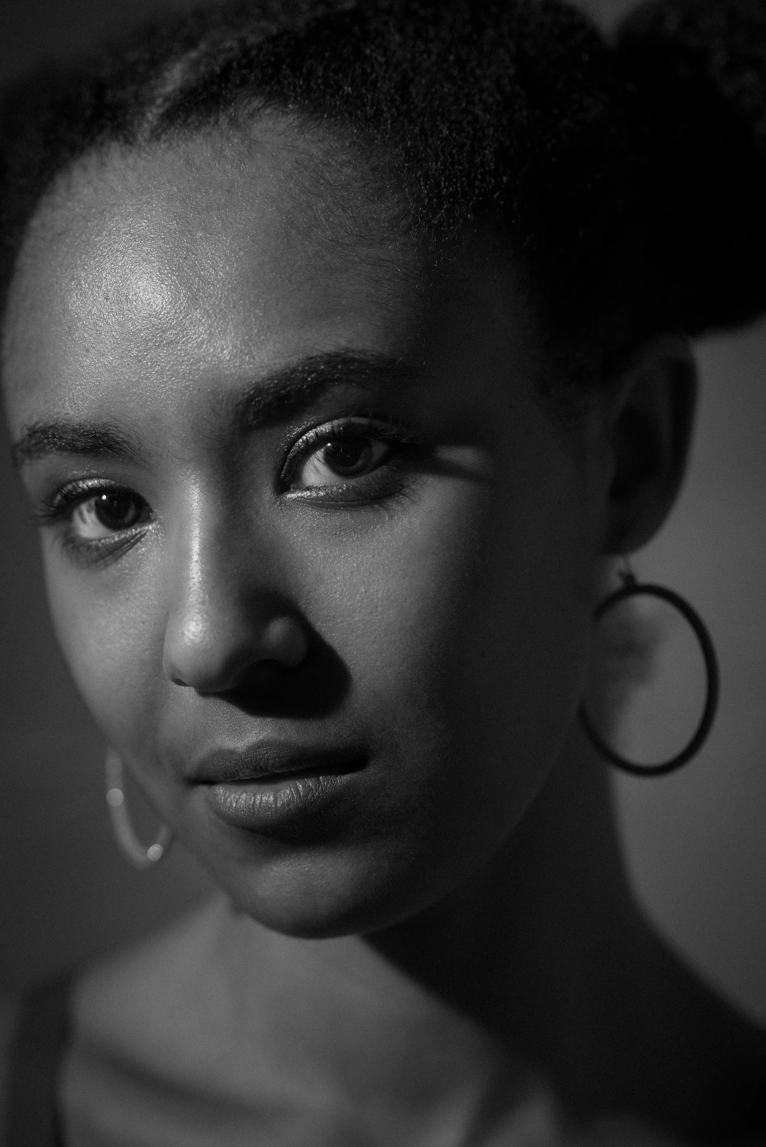 Black and white close-up portrait of a young woman with hoop earrings, looking directly at the camera with a neutral expression.
