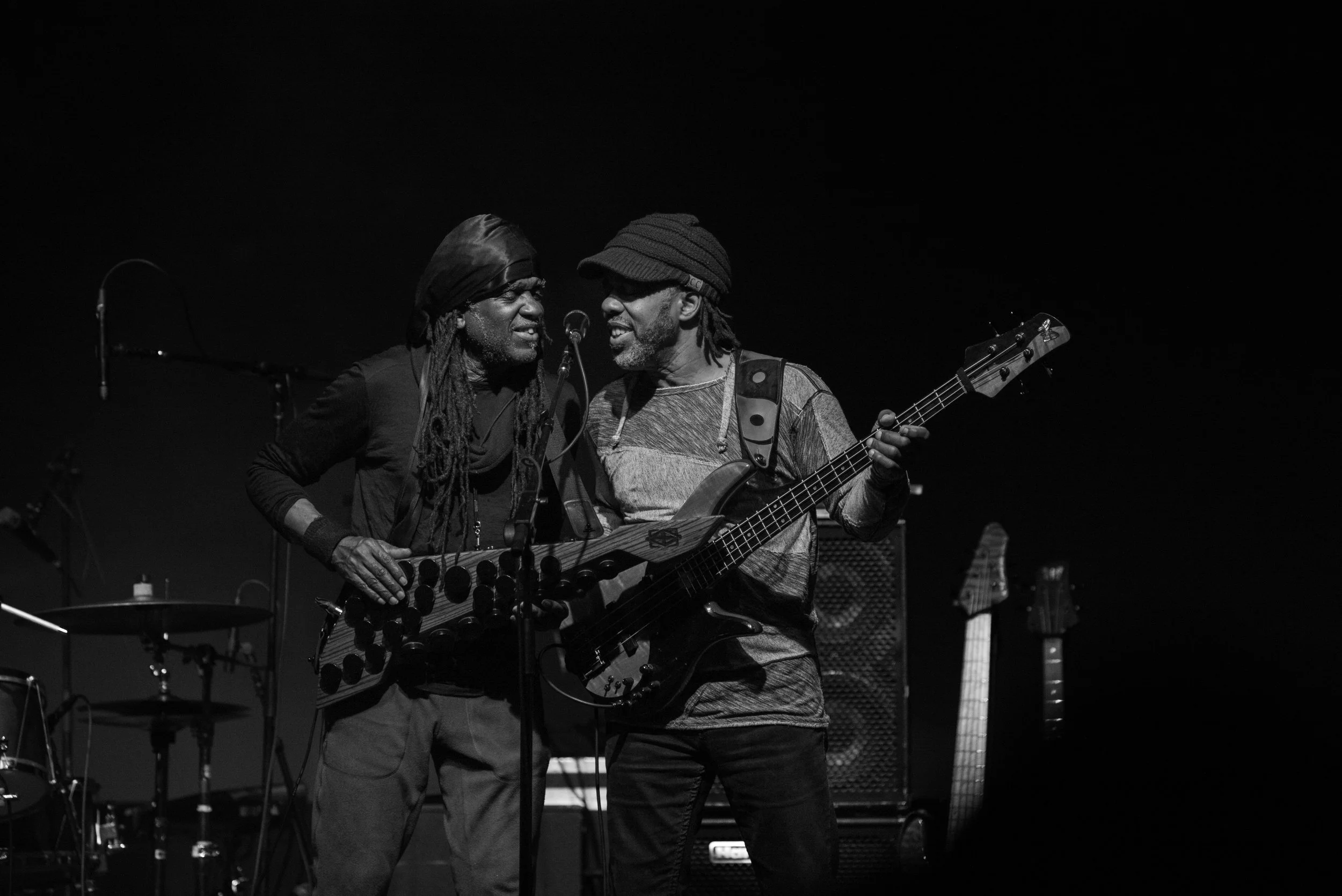 Two male musicians performing on stage with guitars, engaging closely with each other, in a black and white photo.