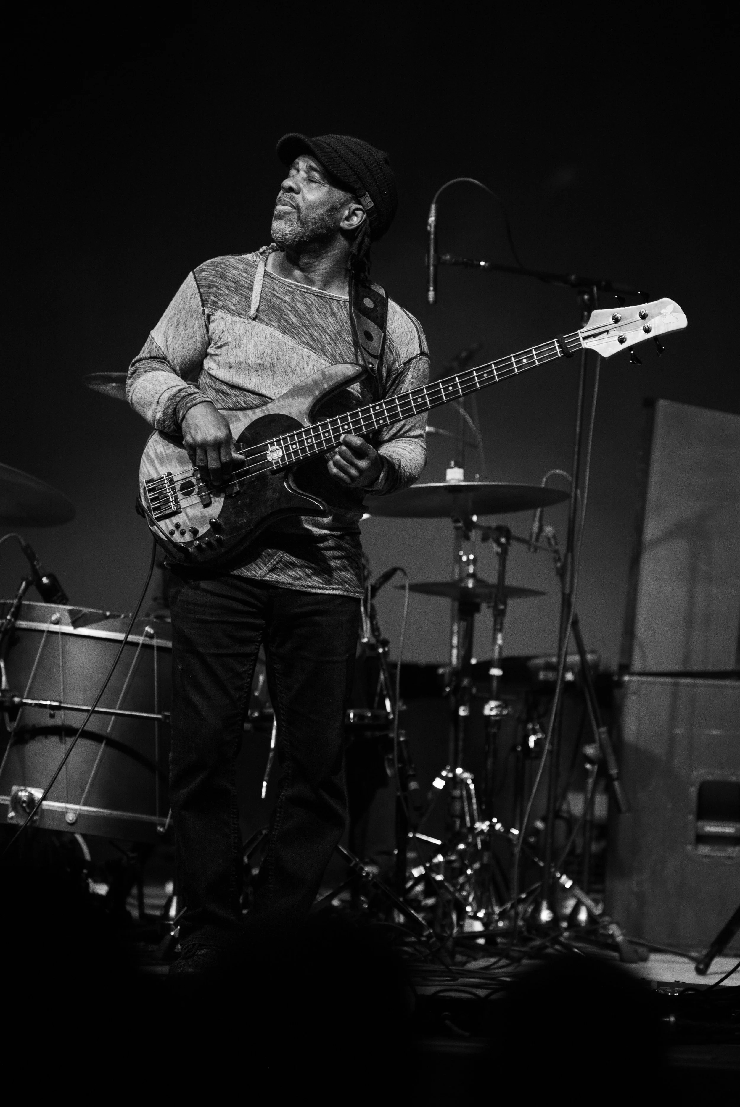 A Black man with a beard playing a bass guitar on stage during a musical performance.