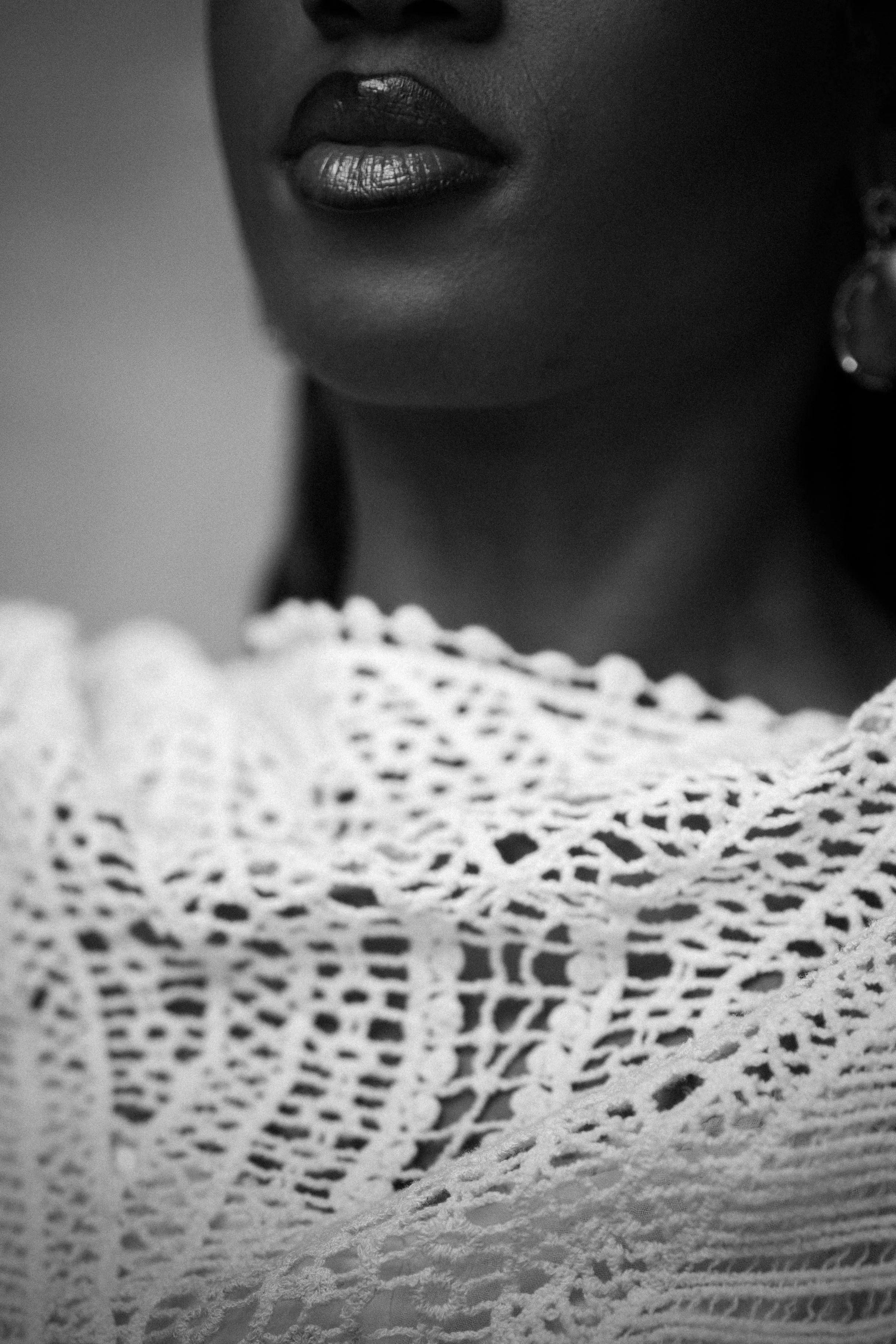 Close-up of a woman's lips and neck, showing glossy lipstick, wearing earrings and a crocheted top.