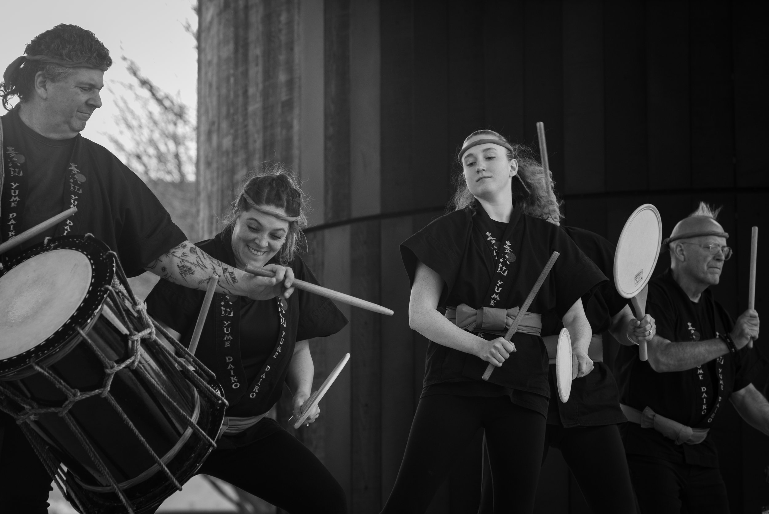 Group of four people playing traditional Japanese drums and percussion instruments outdoors during a performance.