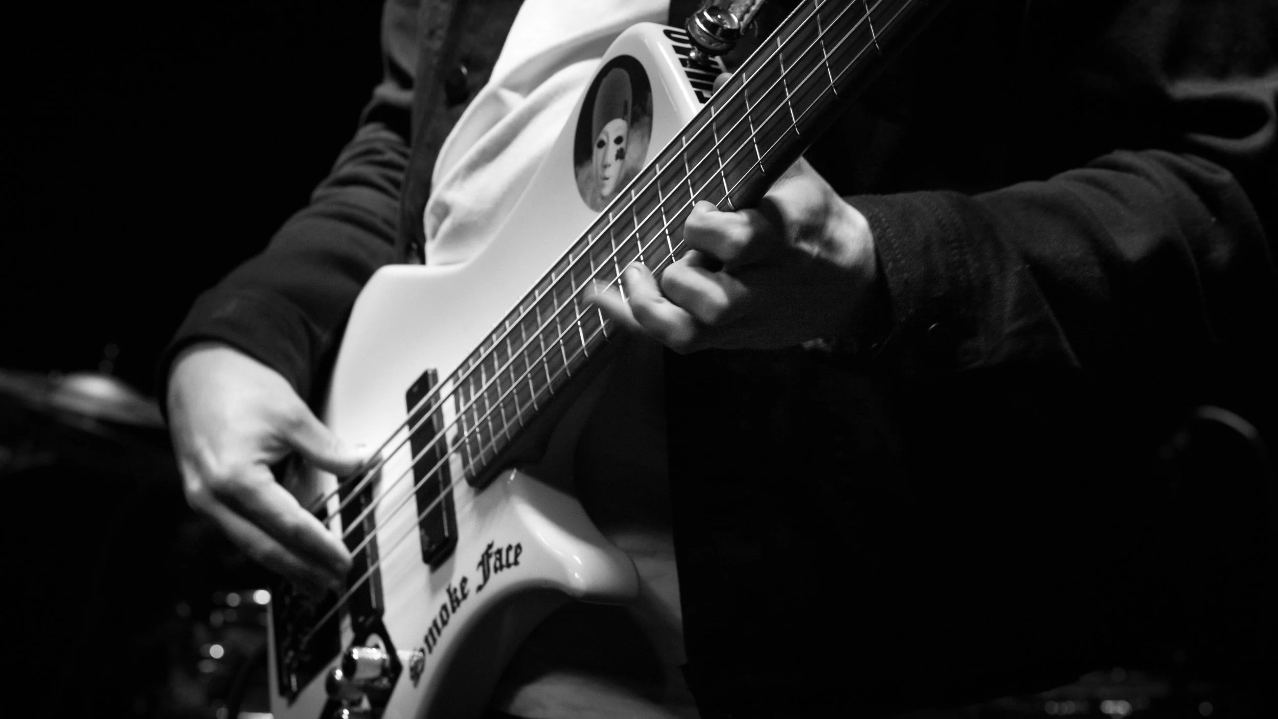 Close-up of a person playing an electric guitar, with a sticker of an alien face on the body, in black and white.