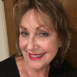 A smiling woman with short, wavy light brown hair and red lipstick, wearing a black top and earrings.