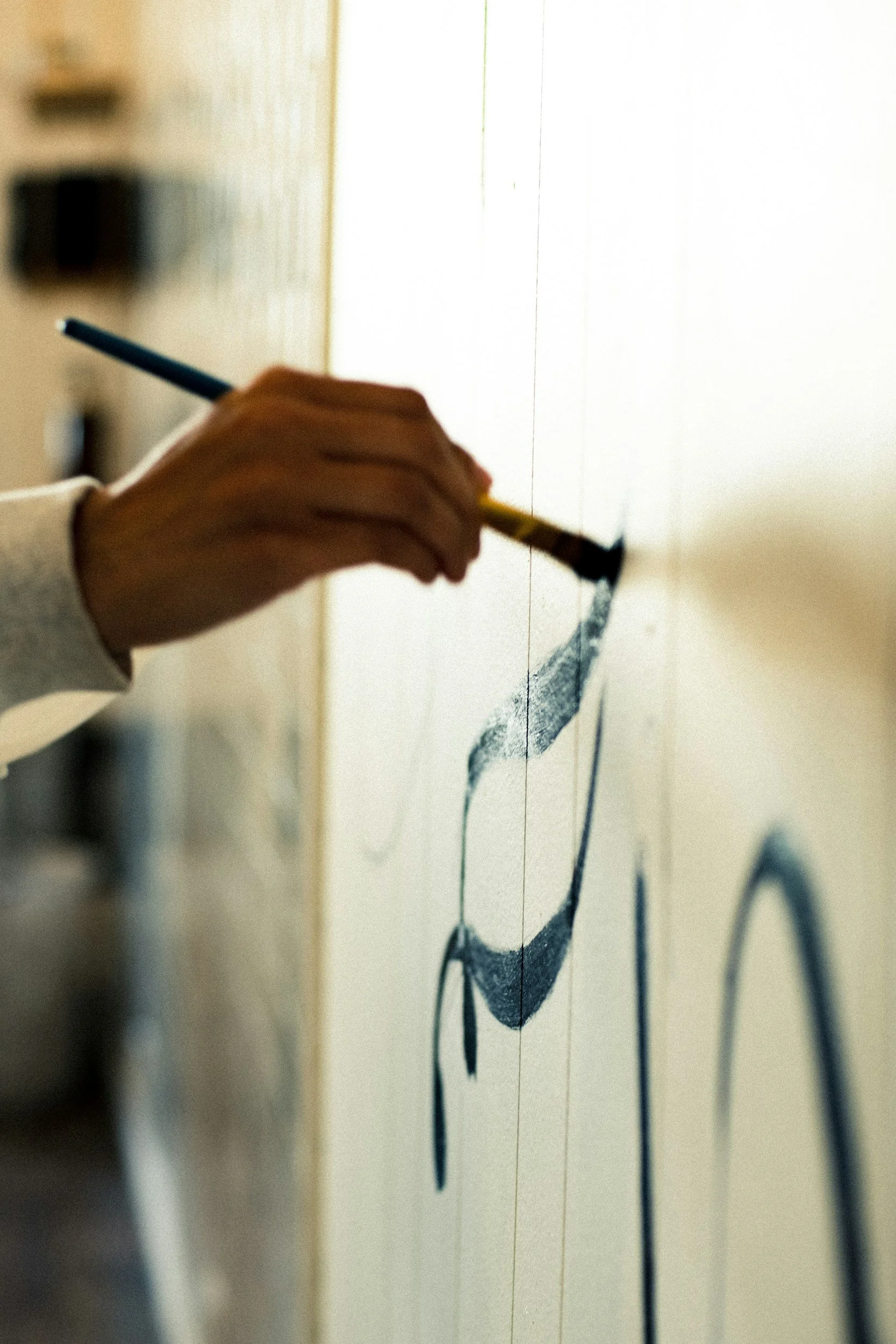 Person painting a black smiley face on a white wall.