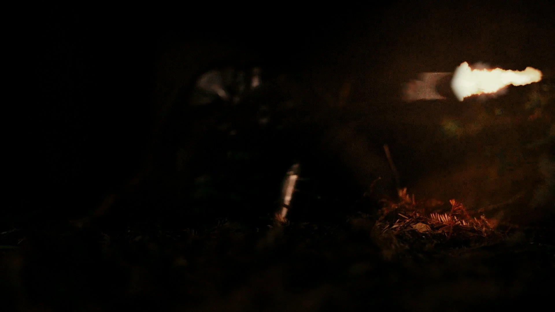 Masked person shooting a sniper rifle at night, illuminated only by the light from the gunshot.