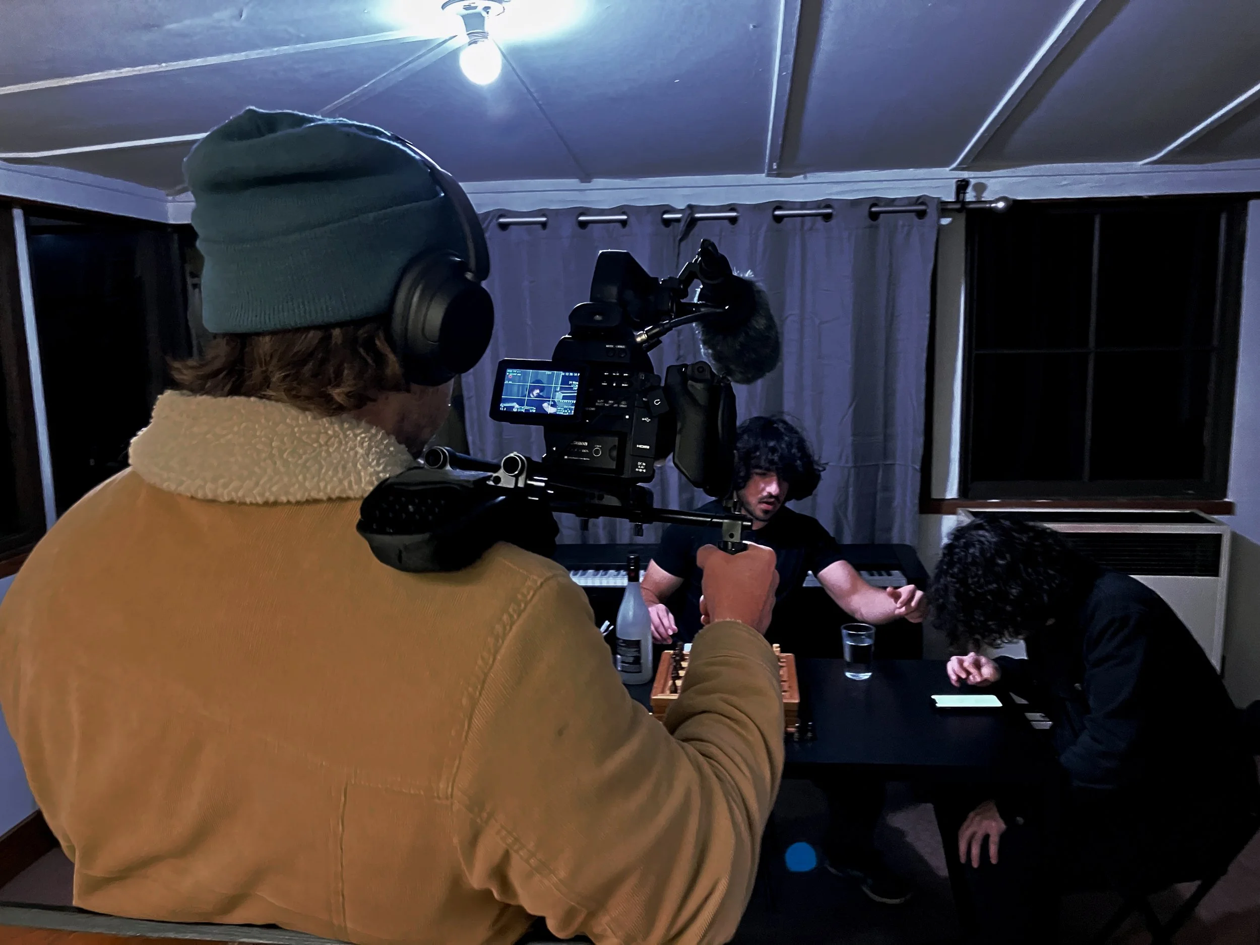 Behind-the-scenes of a director-actor moment, over-the-shoulder shot of a cameraman preparing to film a scene involving a chess game, cinematic film set atmosphere, natural lighting, realistic style.