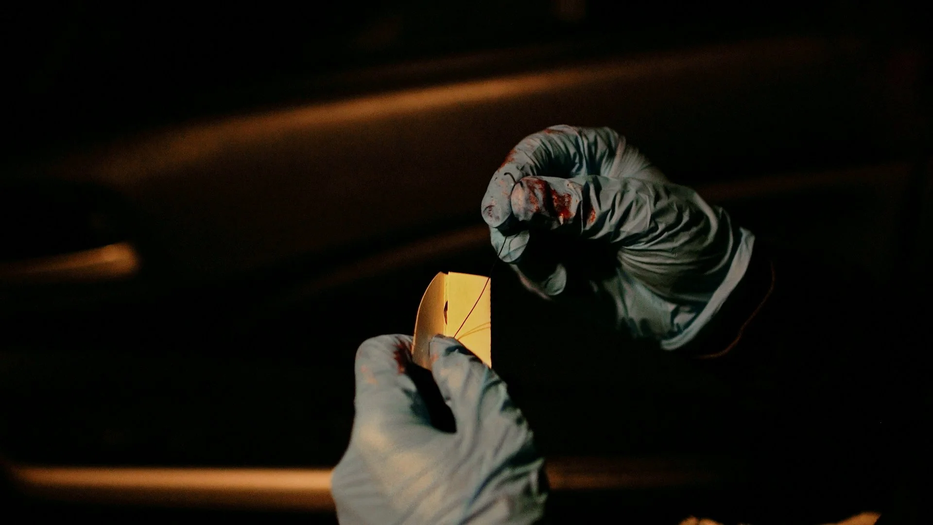 Close-up of bloody plastic gloves holding what appears to be a surgical stitch, in a dark, moody environment, cinematic lighting, high detail, gritty and tense atmosphere.