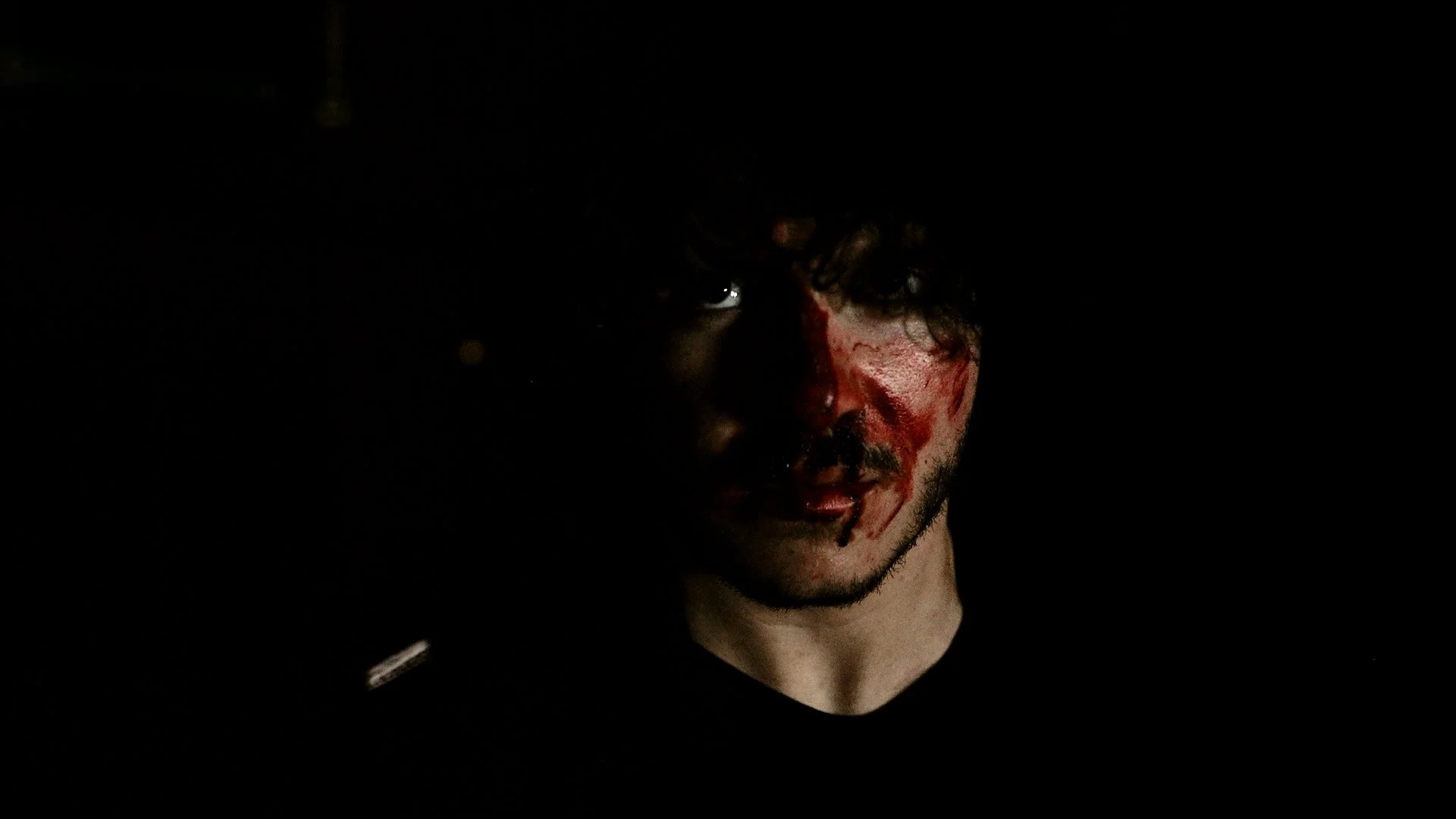 A cinematic close-up of a person with a partially visible face, partially obscured in shadow, blood on their skin, in a dark, moody environment with dramatic lighting and a tense, suspenseful atmosphere.