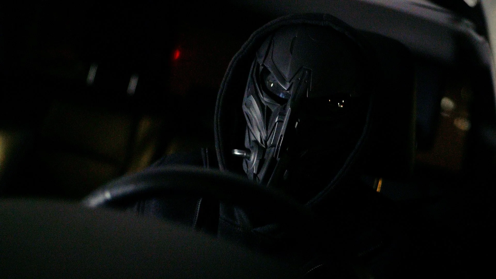 Masked person driving a vehicle at night in a dark environment.