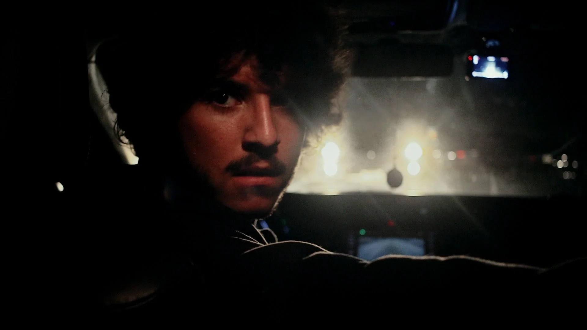 Person reversing as a car approaches in front of them in an intense, dark scene.