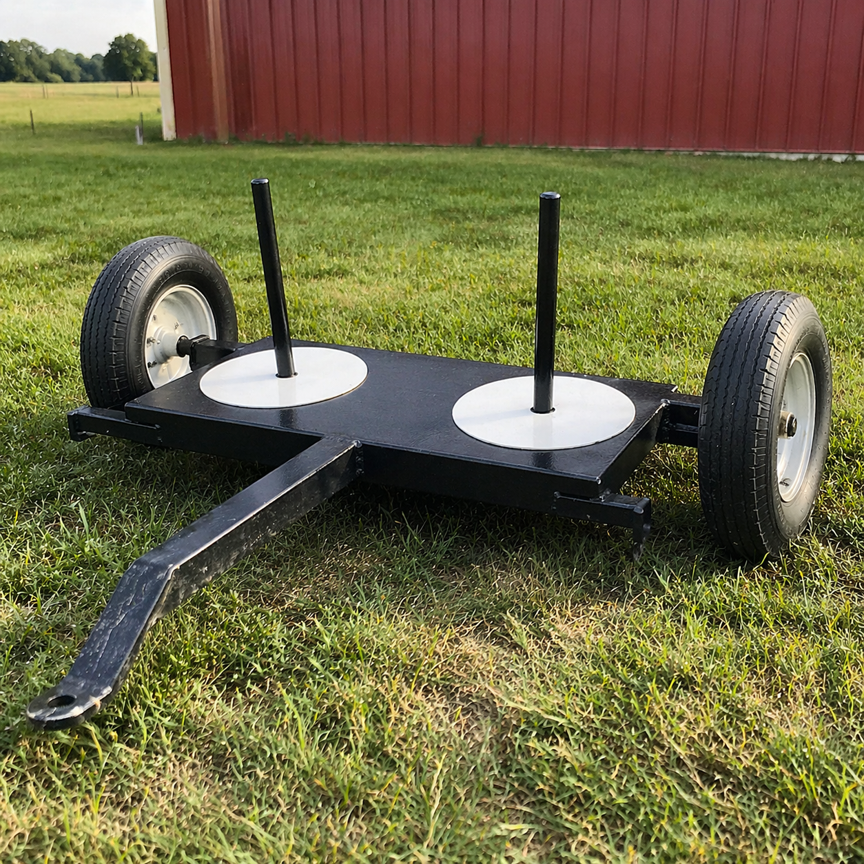 A black cart with two wheels and two vertical poles on a grassy field with a red barn in the background.