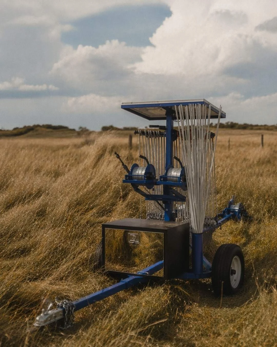 A weather measurement device with an array of metallic rods and sensors is standing in a grassy field under partly cloudy skies.