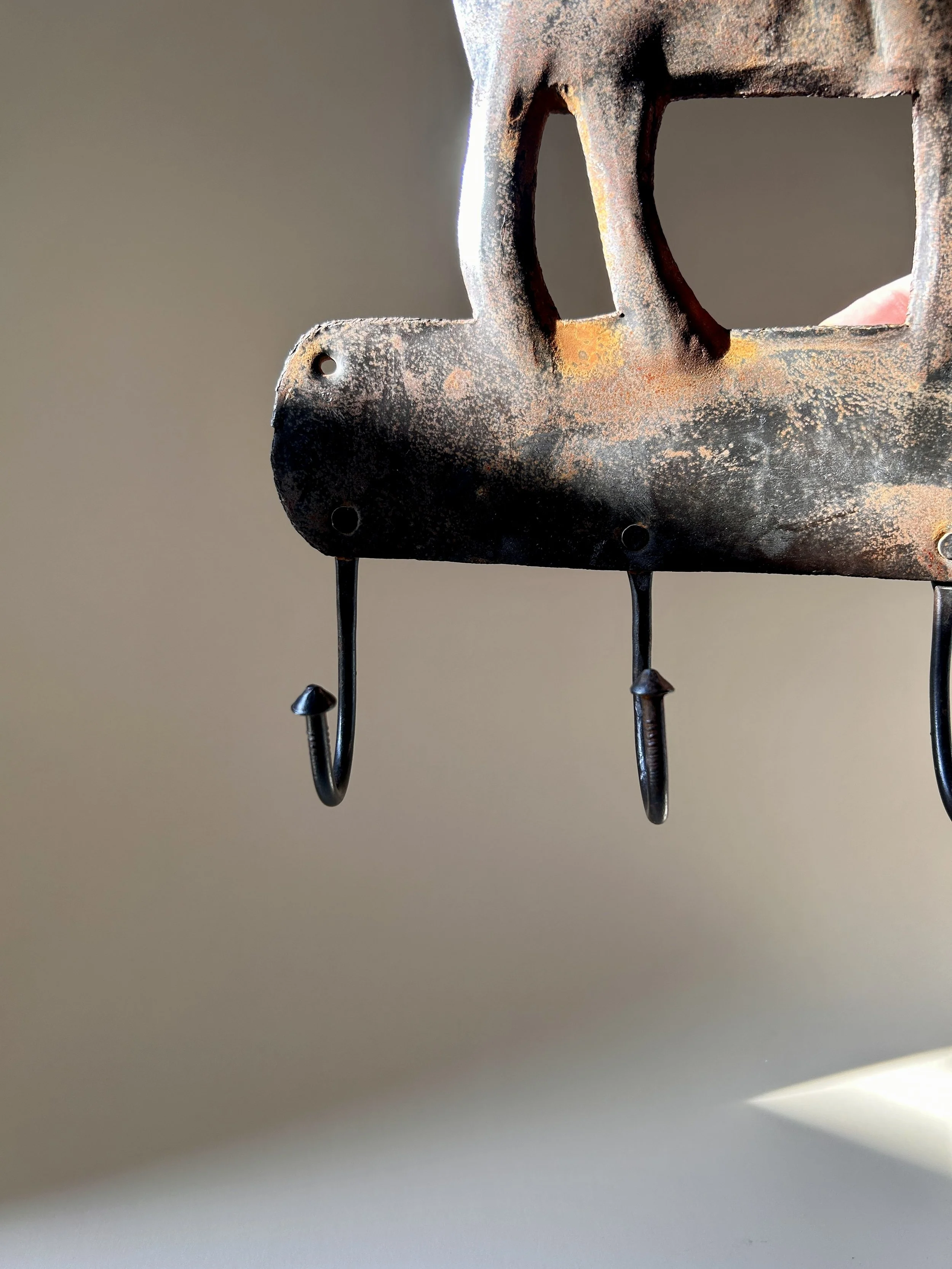 Vintage metal wall hook rack featuring a stylized deer silhouette, four curved hooks, and a heavily aged dark brown and rust colored surface.