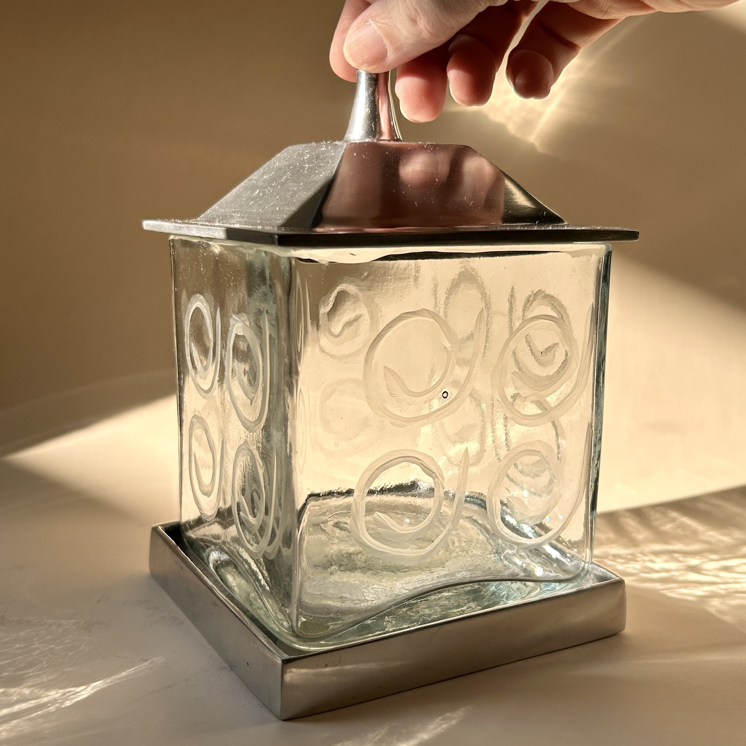 Contemporary square clear glass canisters with etched spiral patterns, silver-tone metal bases, and peaked metal lids in two different heights.