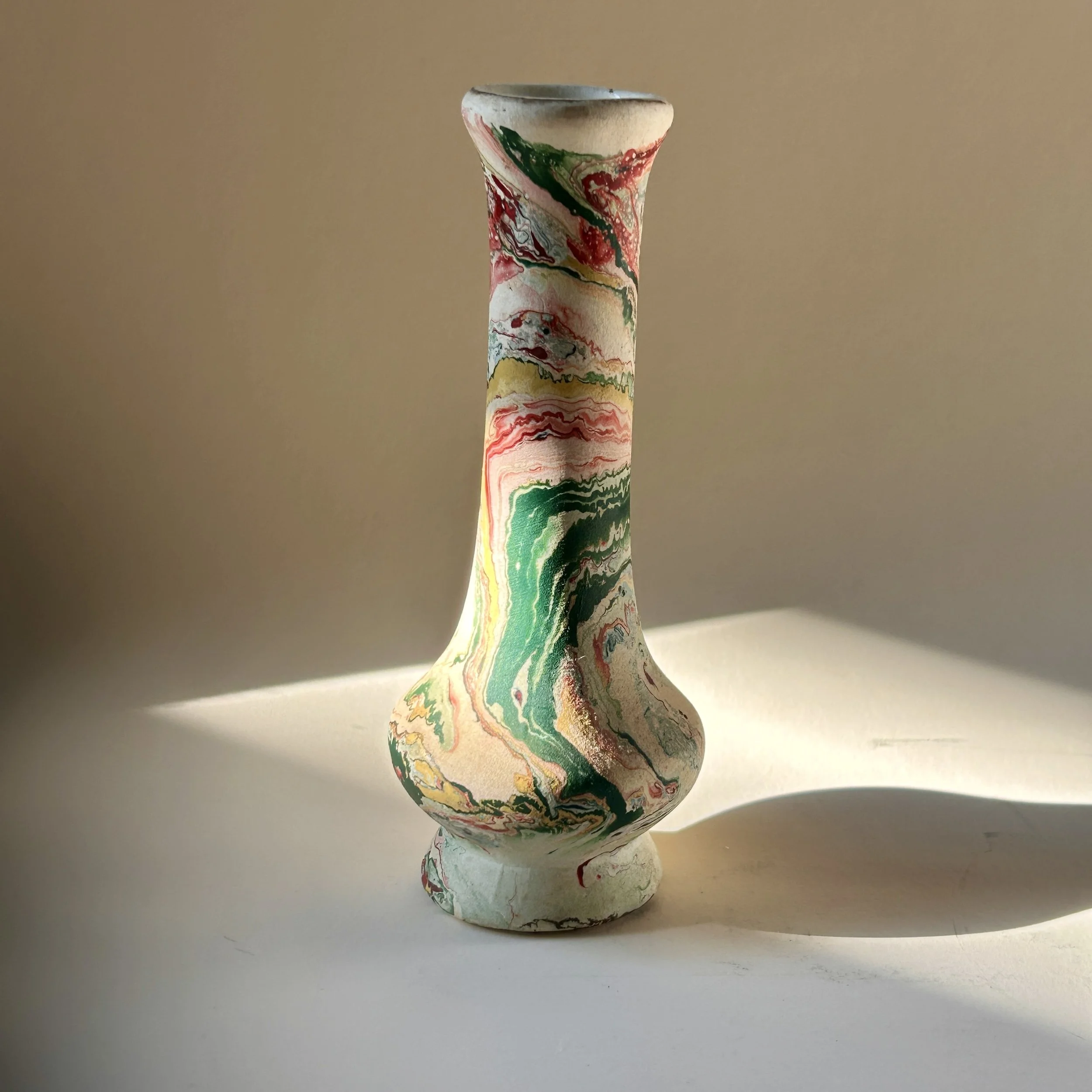 Slender vintage pottery bud vase with cream surface and swirling marbled patterns in green, coral, red, ochre, gray and black.