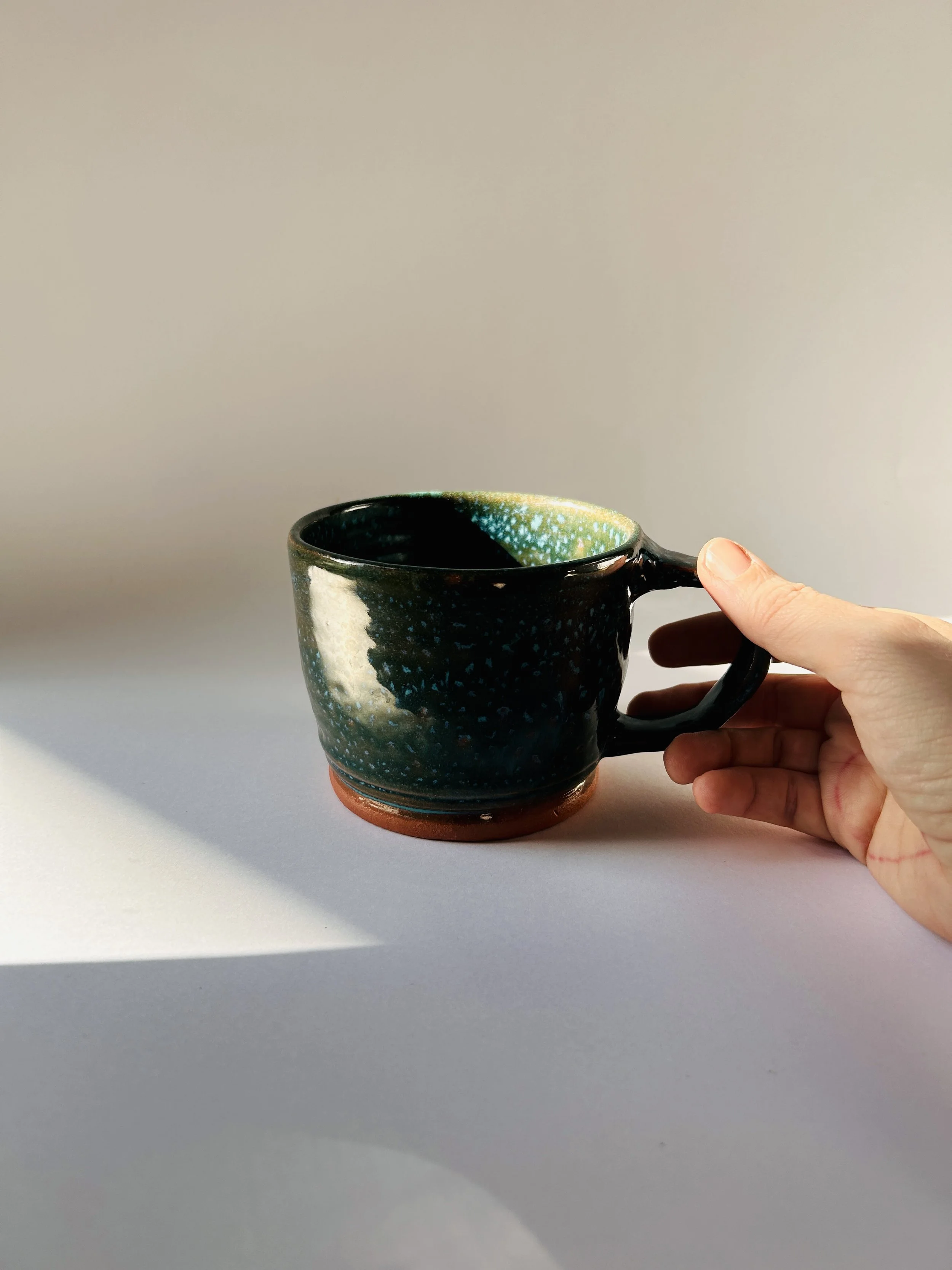 handmade speckled ceramic mug with dark teal glaze and terracotta base