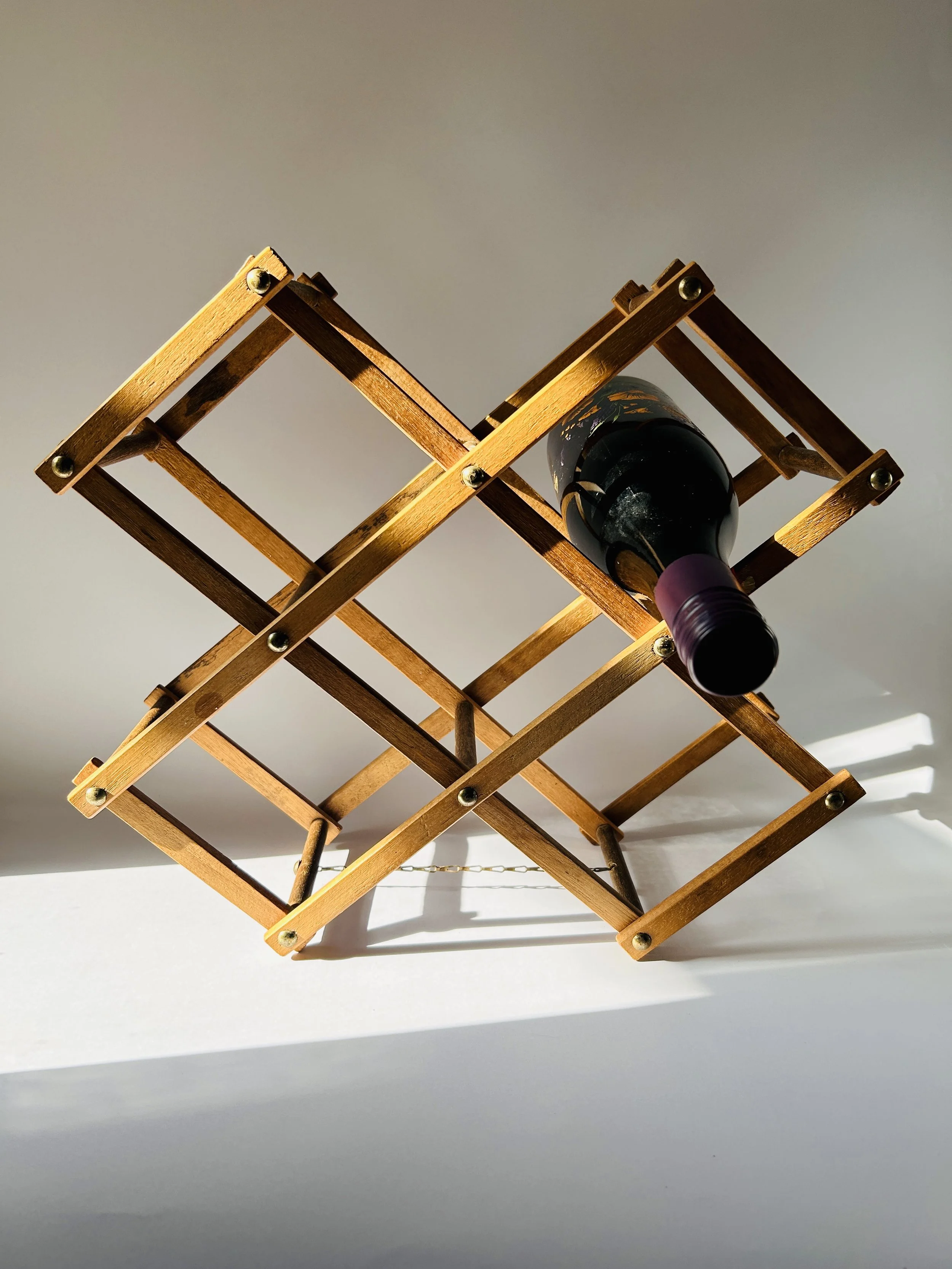 Mid-century expandable wooden wine rack holding five bottles, folding geometric bar storage
