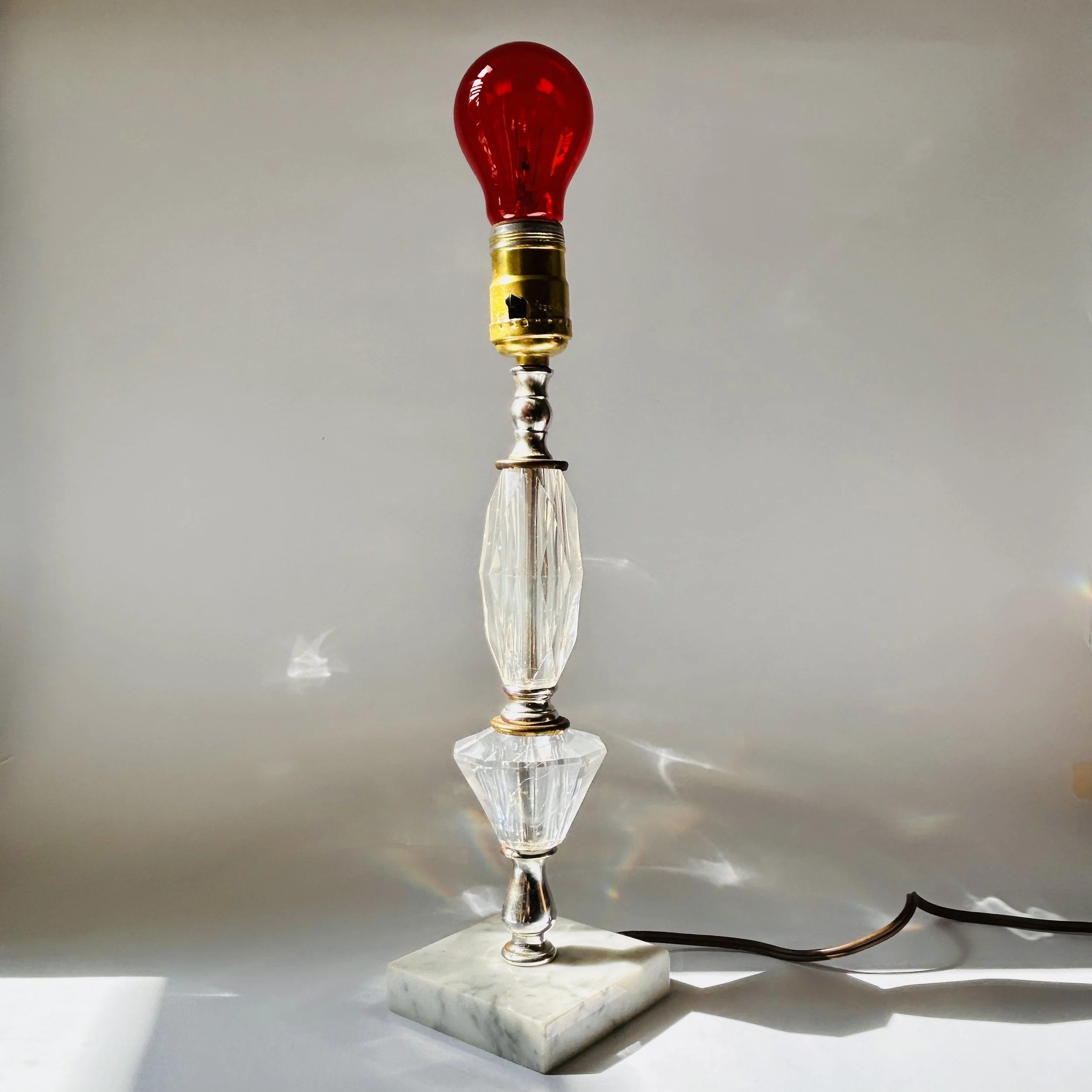 Vintage table lamp with faceted clear crystal-look elements, silver-tone metal accents, pale marble square base, and exposed red bulb.