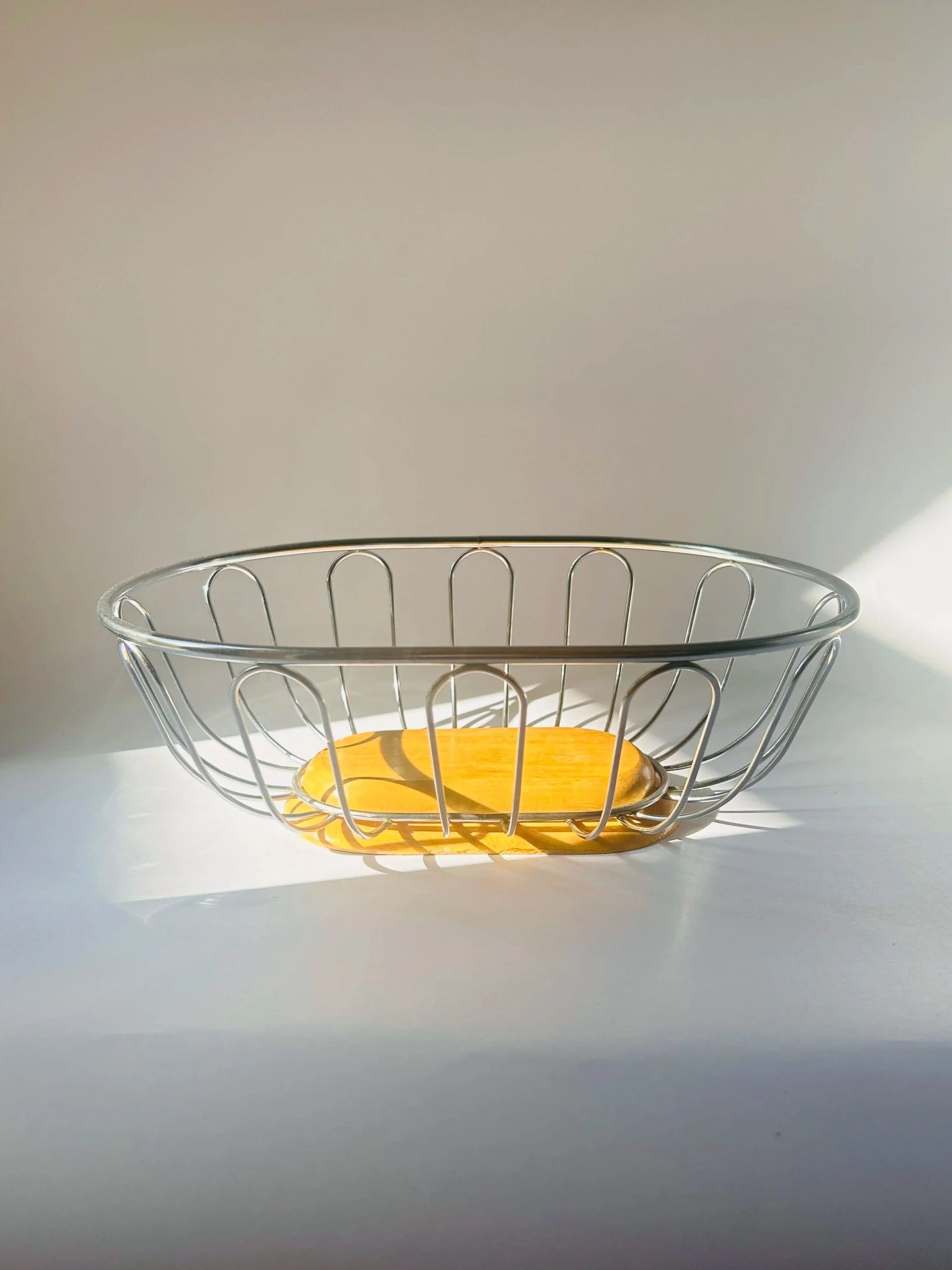 Modern stainless steel wire basket with wooden base, minimalist fruit bowl on countertop