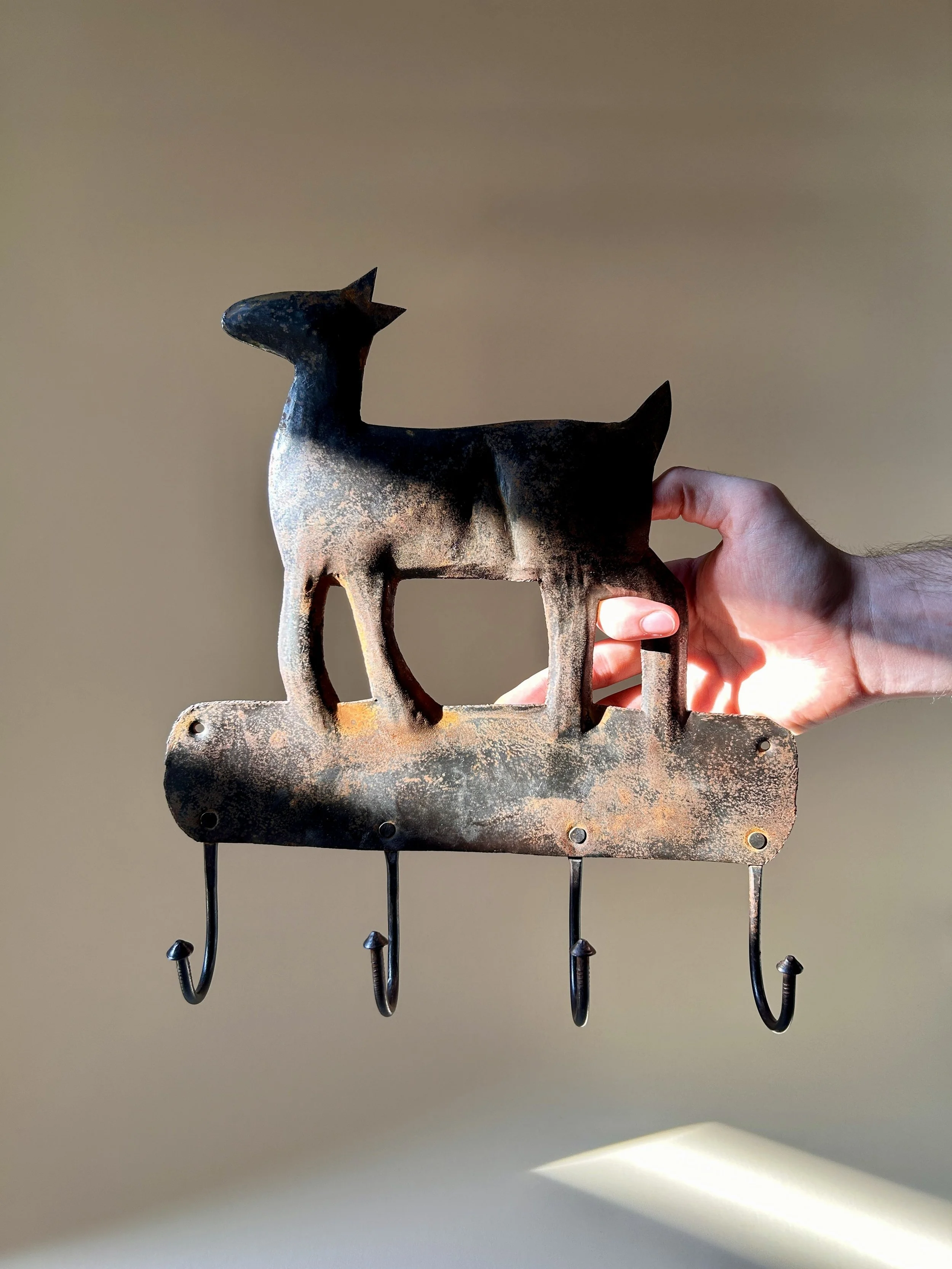 Vintage metal wall hook rack featuring a stylized deer silhouette, four curved hooks, and a heavily aged dark brown and rust colored surface.