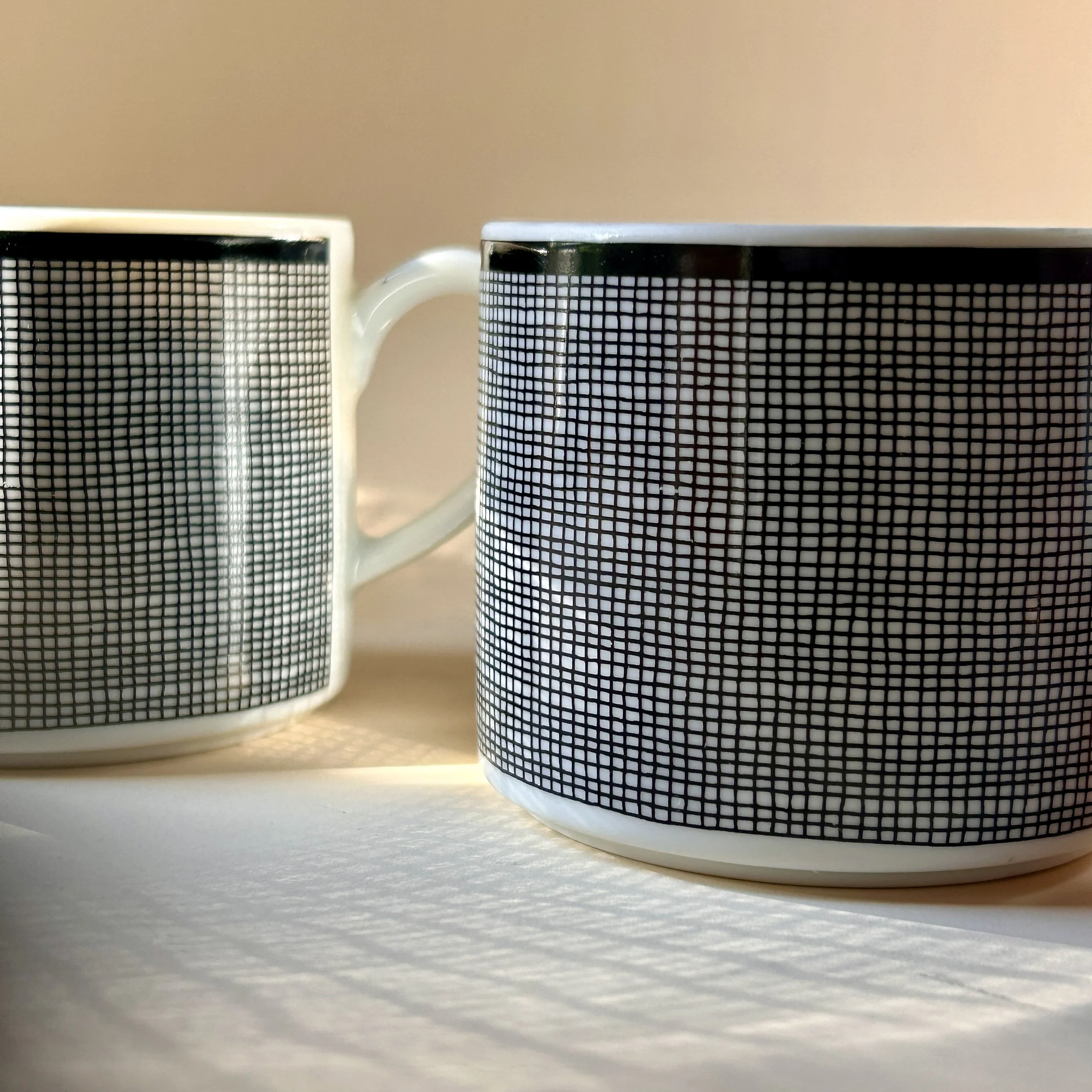 Set of four white Nancy Calhoun Chambray porcelain mugs with fine black grid pattern, black rim and white handles.