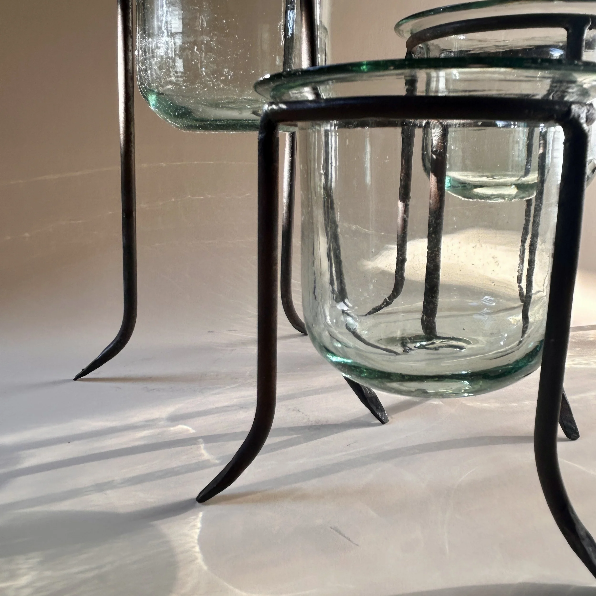 Set of three clear handblown glass tealight holders in dark iron tripod stands with curved legs, shown in graduated heights.
