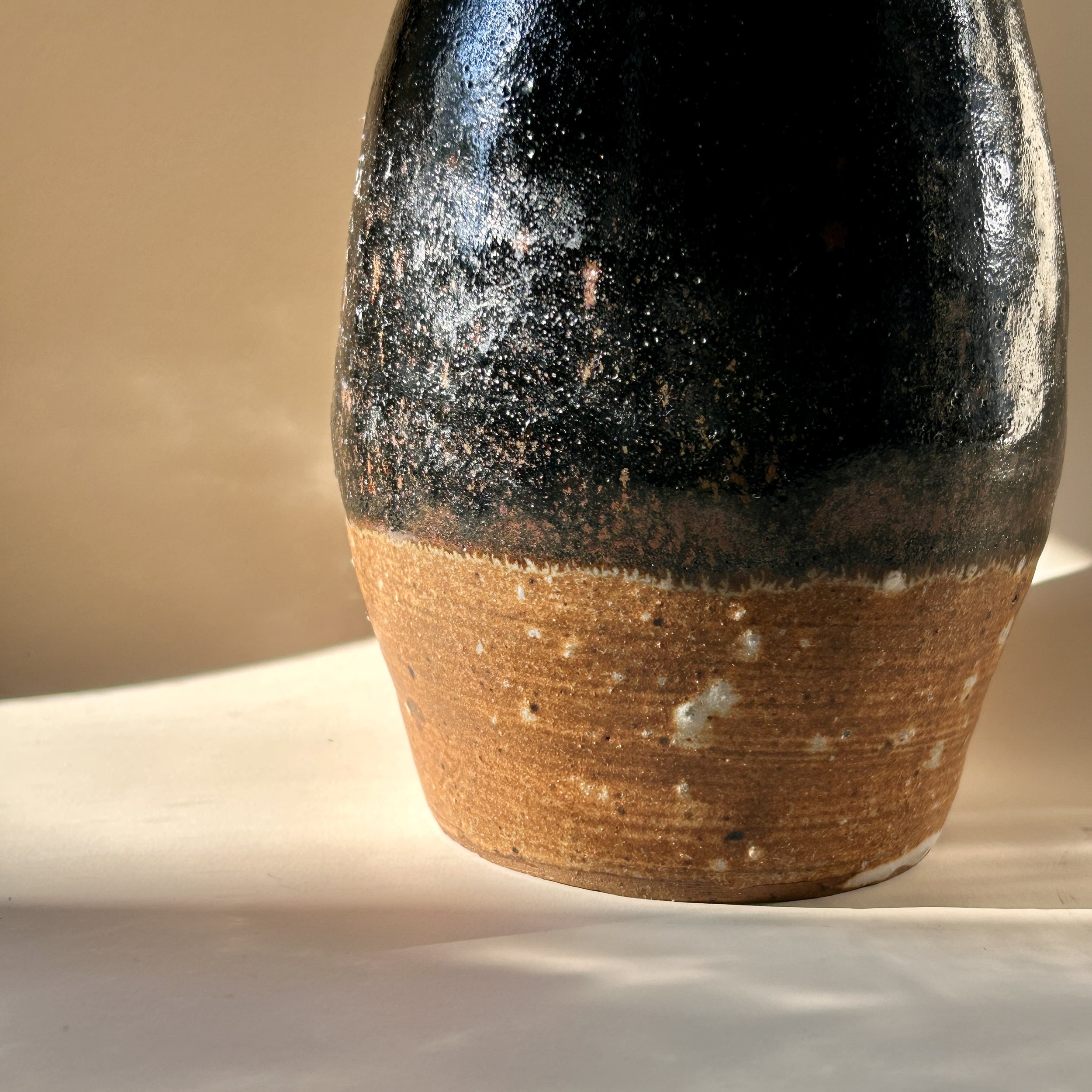 Signed 1989 studio pottery vessel with glossy black tenmoku-style glaze, exposed brown stoneware clay and small bud vase opening.