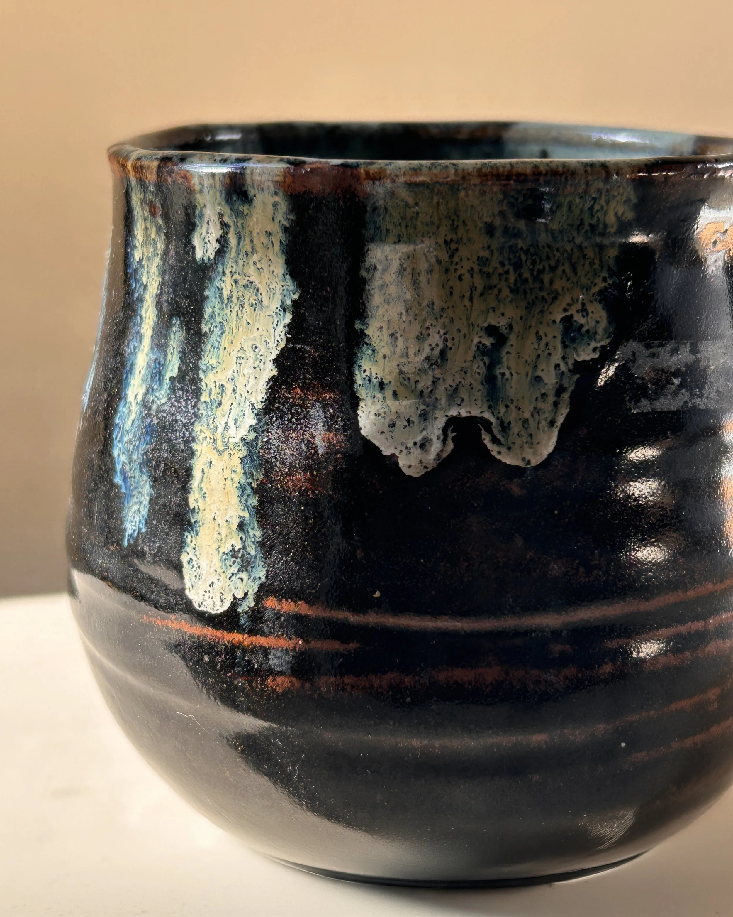 Signed handmade studio pottery vessel with glossy black glaze, rust-colored bands and cascading cream and blue green glaze decoration.