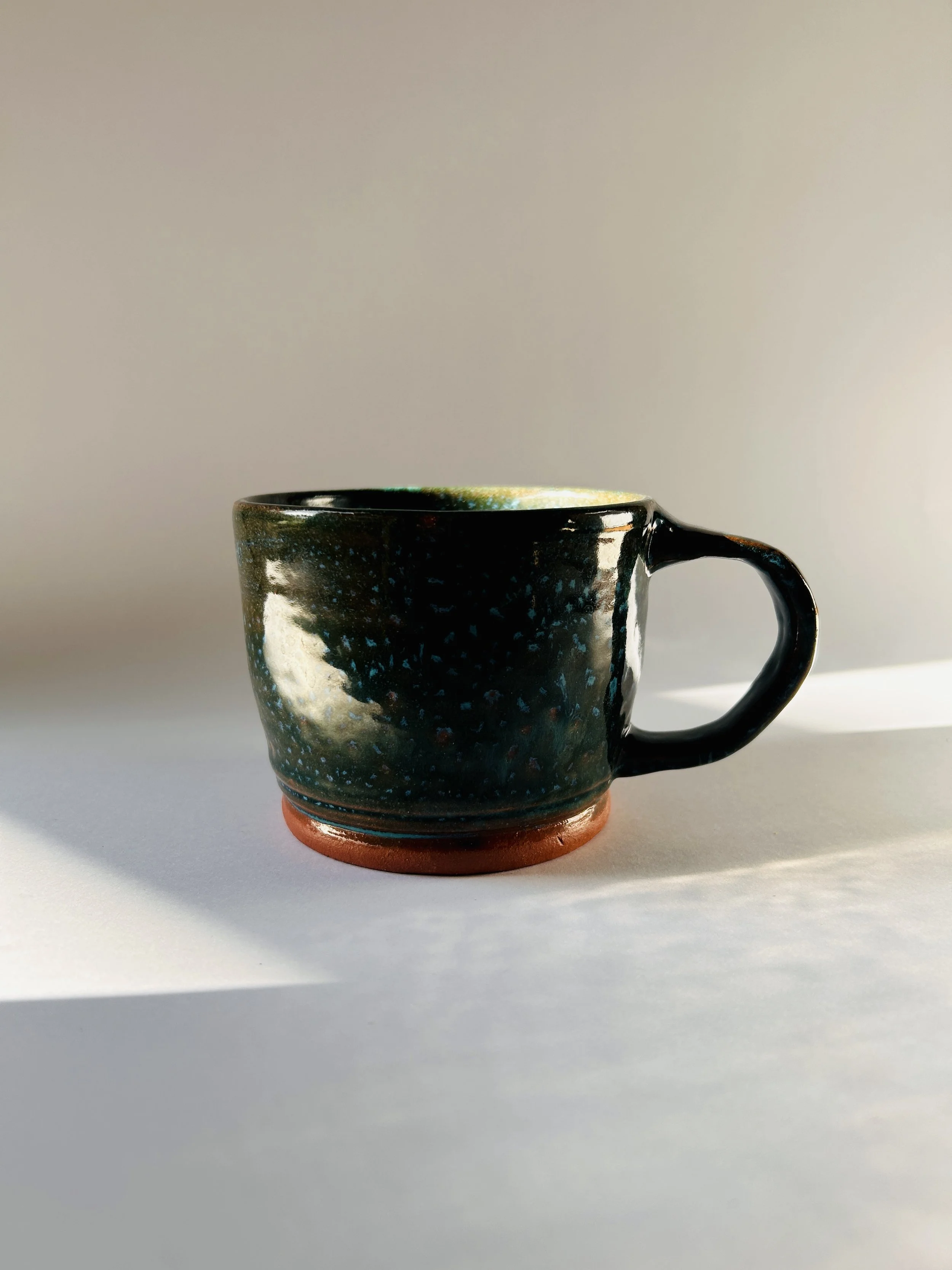 handmade speckled ceramic mug with dark teal glaze and terracotta base