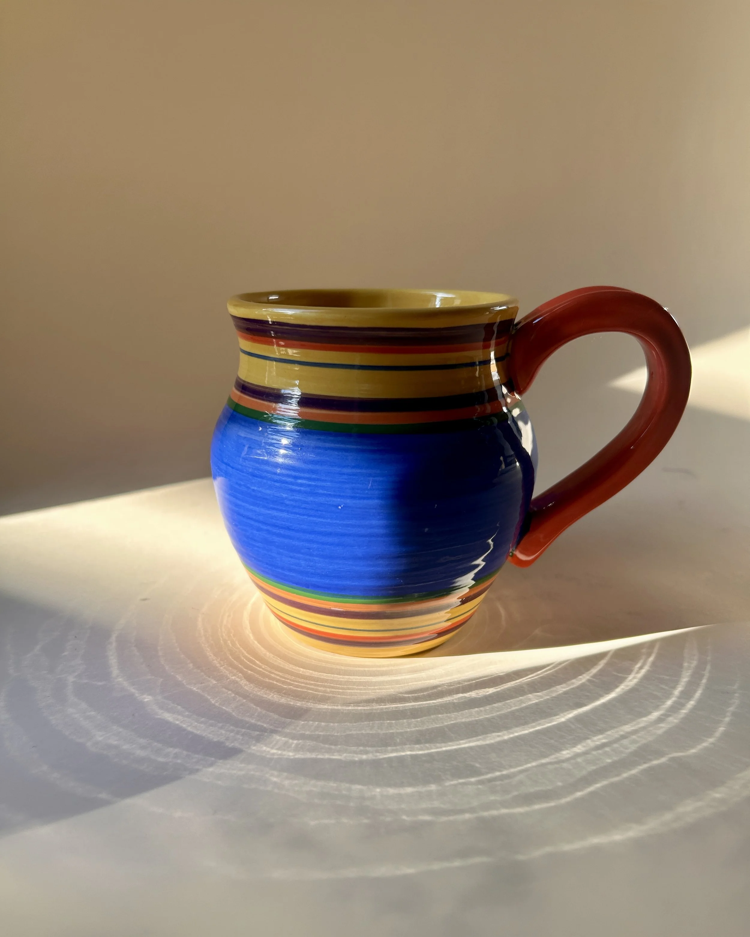 Set of three colorful Pacific Rim Santa Fe stoneware mugs with hand-painted multicolor stripes and contrasting handles and interiors.