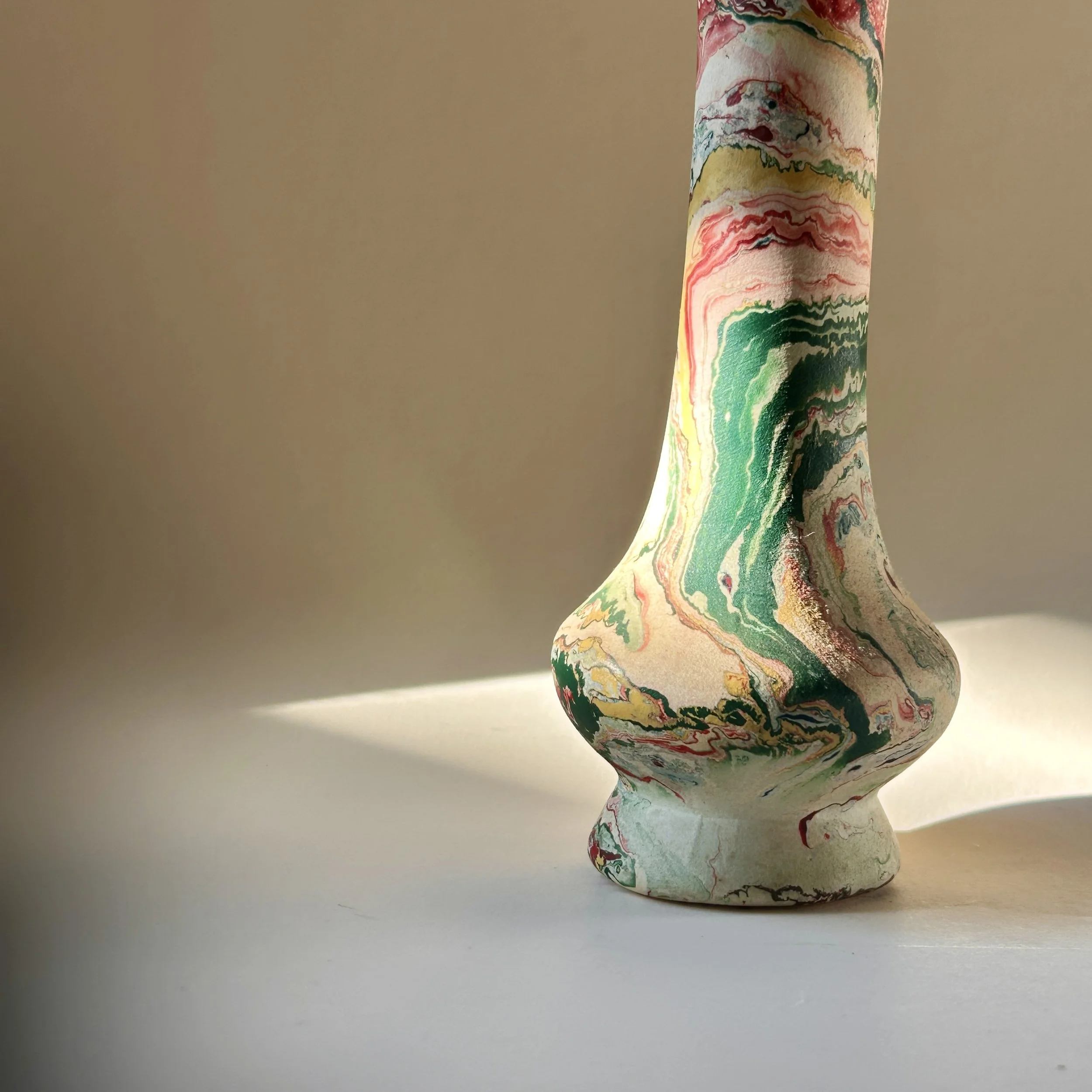 Slender vintage pottery bud vase with cream surface and swirling marbled patterns in green, coral, red, ochre, gray and black.