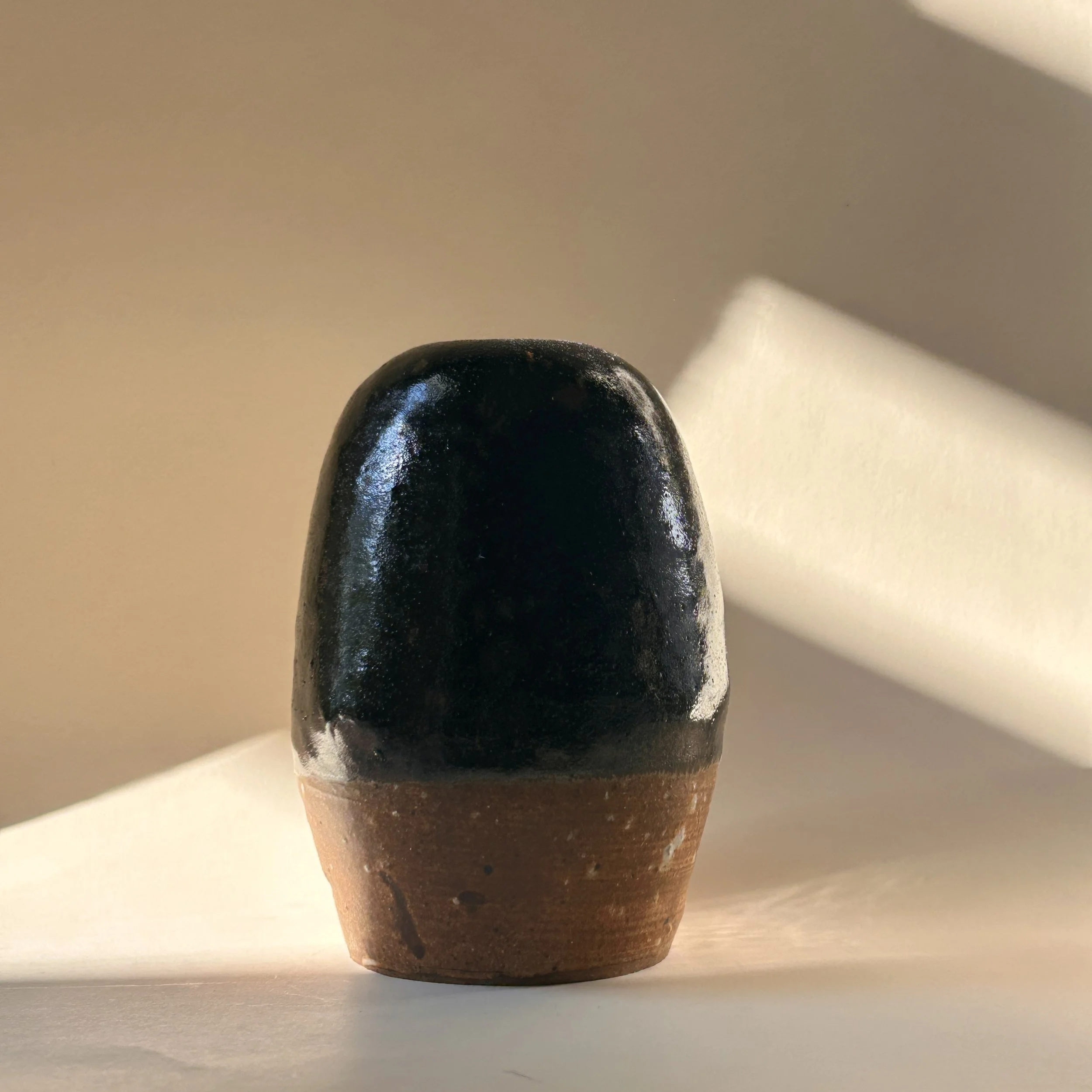 Signed 1989 studio pottery vessel with glossy black tenmoku-style glaze, exposed brown stoneware clay and small bud vase opening.