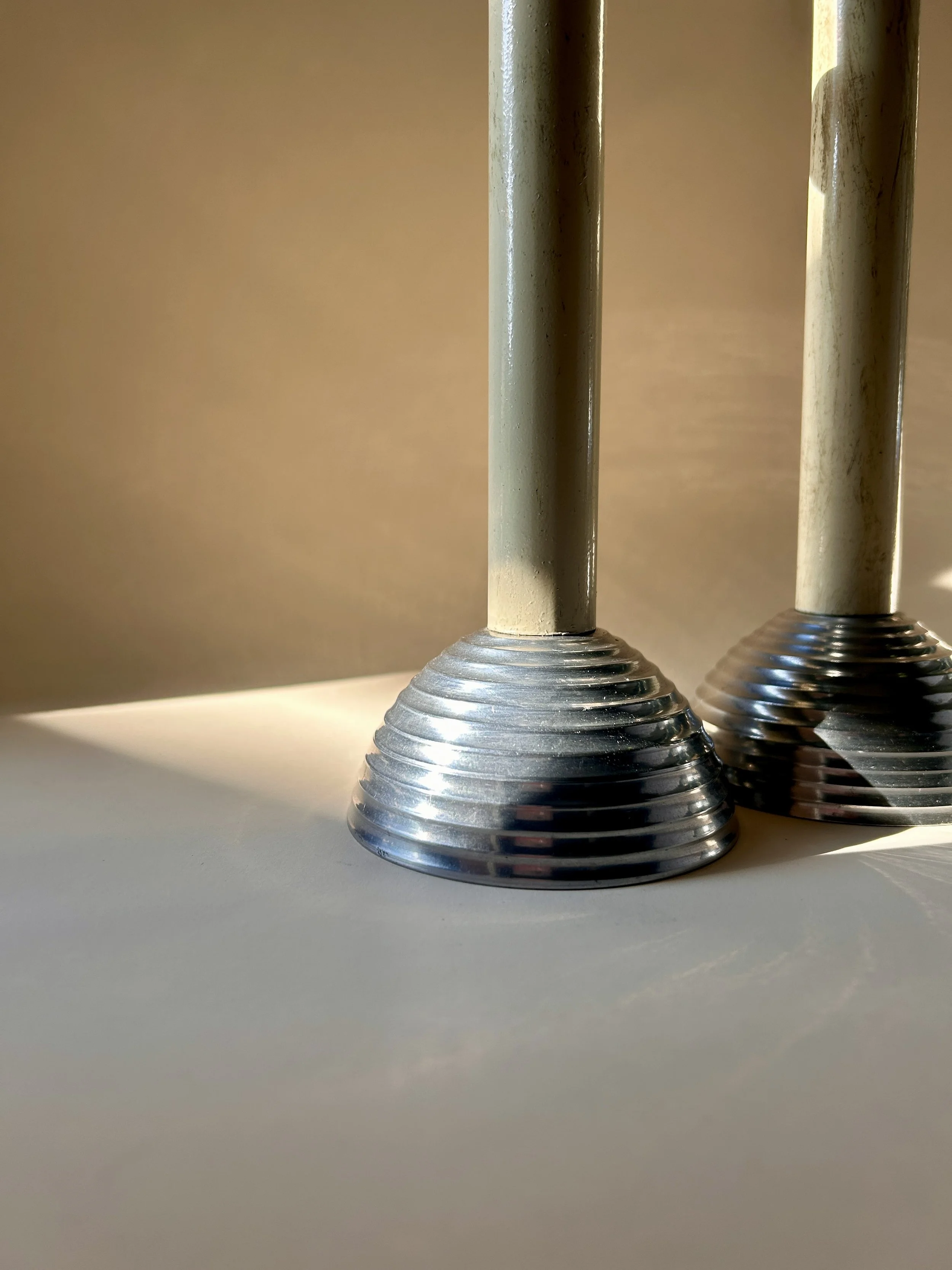 Pair of tall vintage taper candlesticks with slender neutral-colored columns and polished silver tone stepped ribbed bases and candle cups.