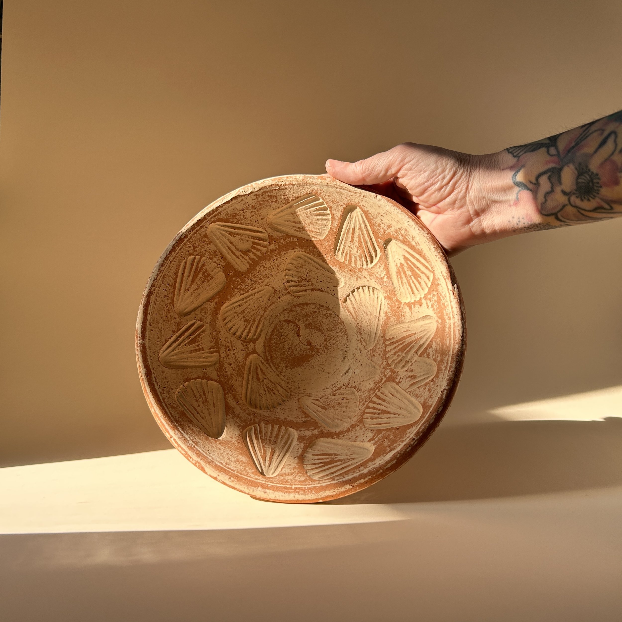Shallow terracotta pottery bowl with raised scallop shell motifs and distressed chalky white finish over warm red clay.
