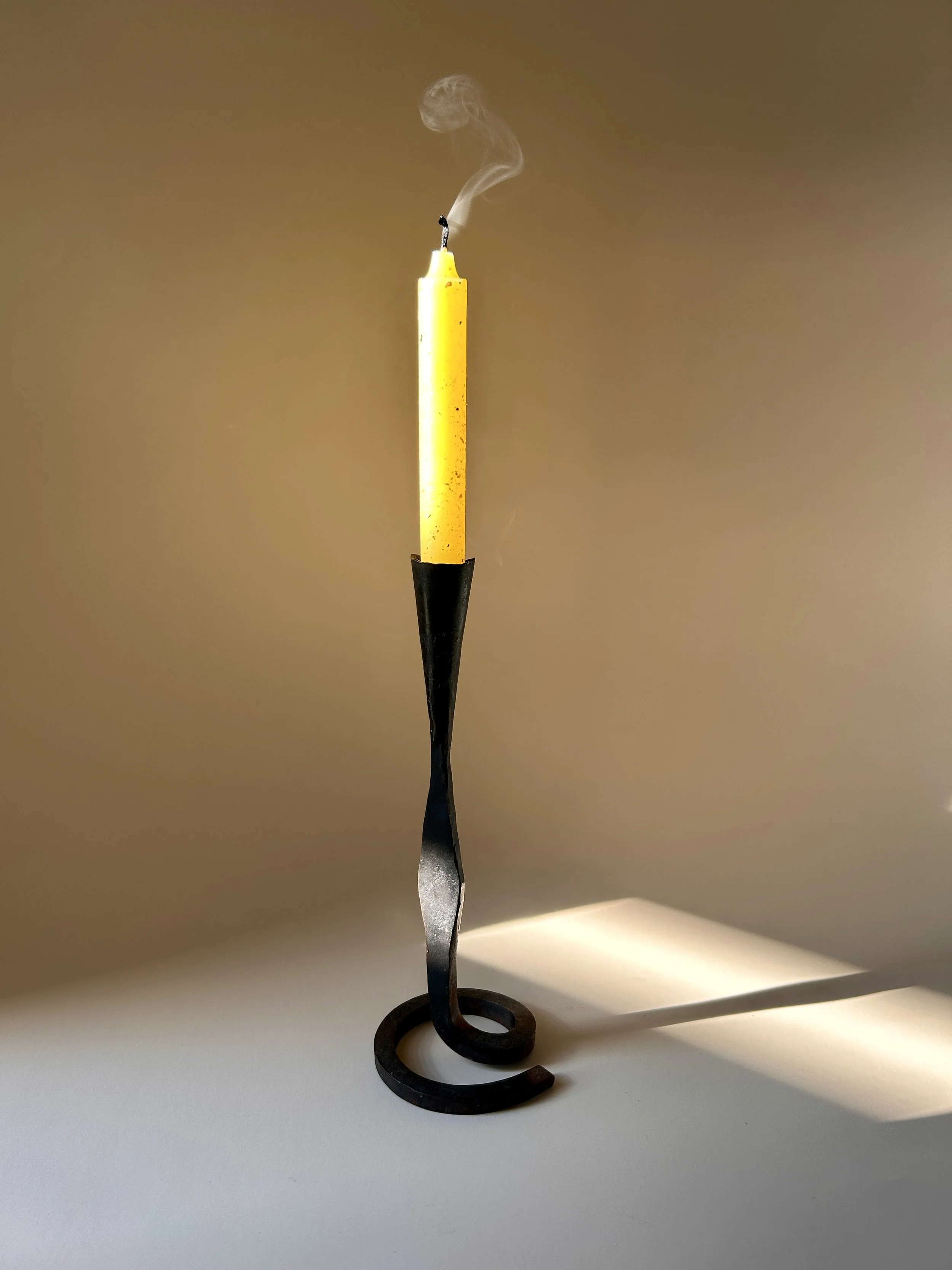 Sculptural hand forged black iron taper candlestick with a curled spiral base, slender twisted stem, and flared candle cup.